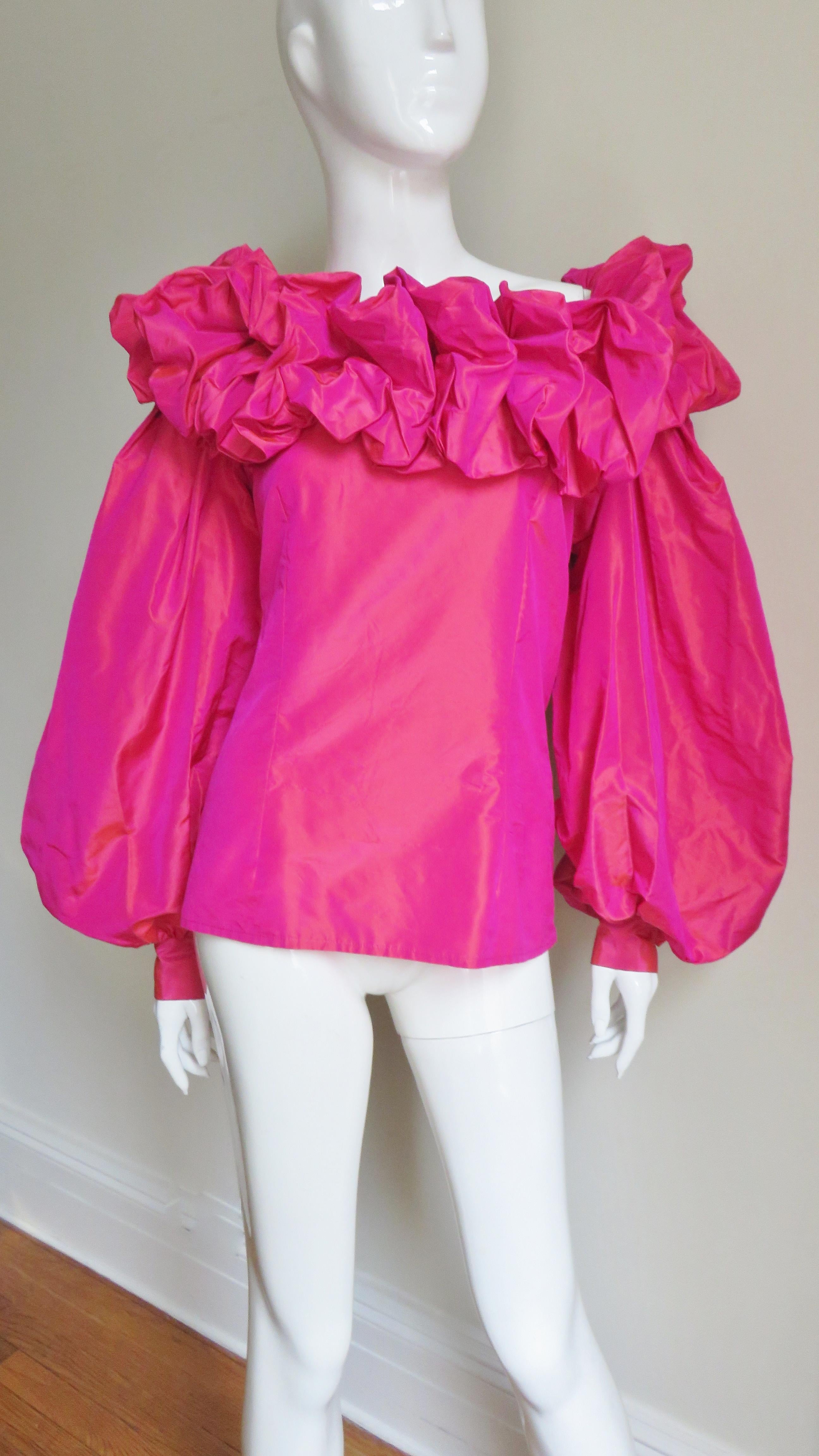 A gorgeous iridescent magenta off shoulder blouse, shirt, top from Guy Laroche.  It has a ruffled collar revealing the tops of the shoulders and full balloon sleeves with self covered button cuffs.  It has a side zipper and is new with tags.
Fits