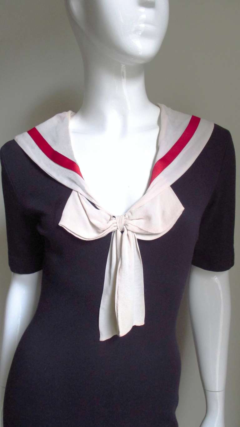 An adorable navy body conscious sailor dress from Moschino in a heavy cotton/spandex knit.  It is short sleeved with a sailor collar that ties in the front with a bow in off white silk with a red grosgrain ribbon trim.
Excellent condition.

Bust 