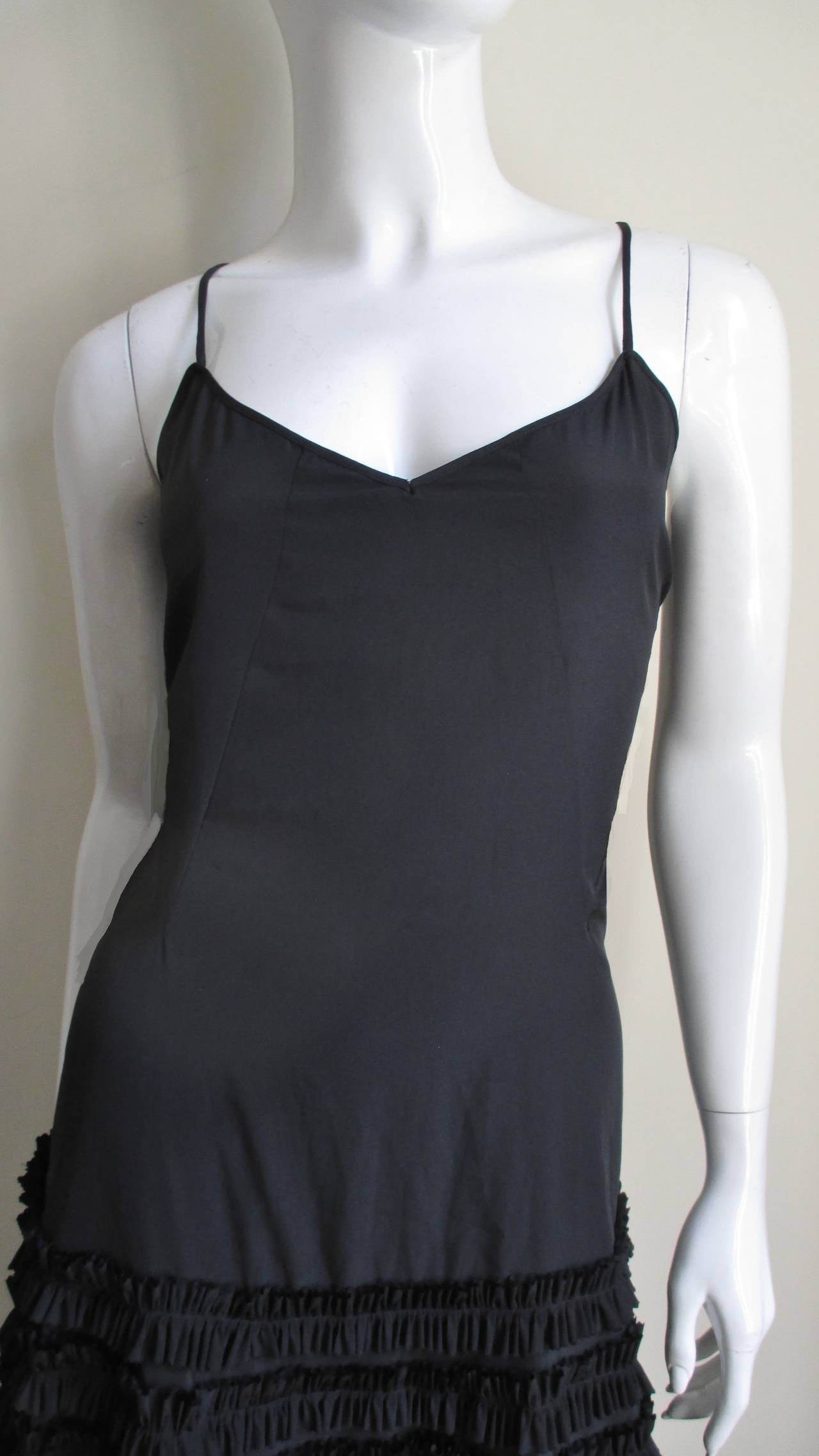 An adorable black silk slip dress from an early collection of Alexander McQueen's. It has spaghetti straps, a sweetheart neckline and a low cut back. It is semi fitted through a the upper hips at which point rows of center stitched small ruffles