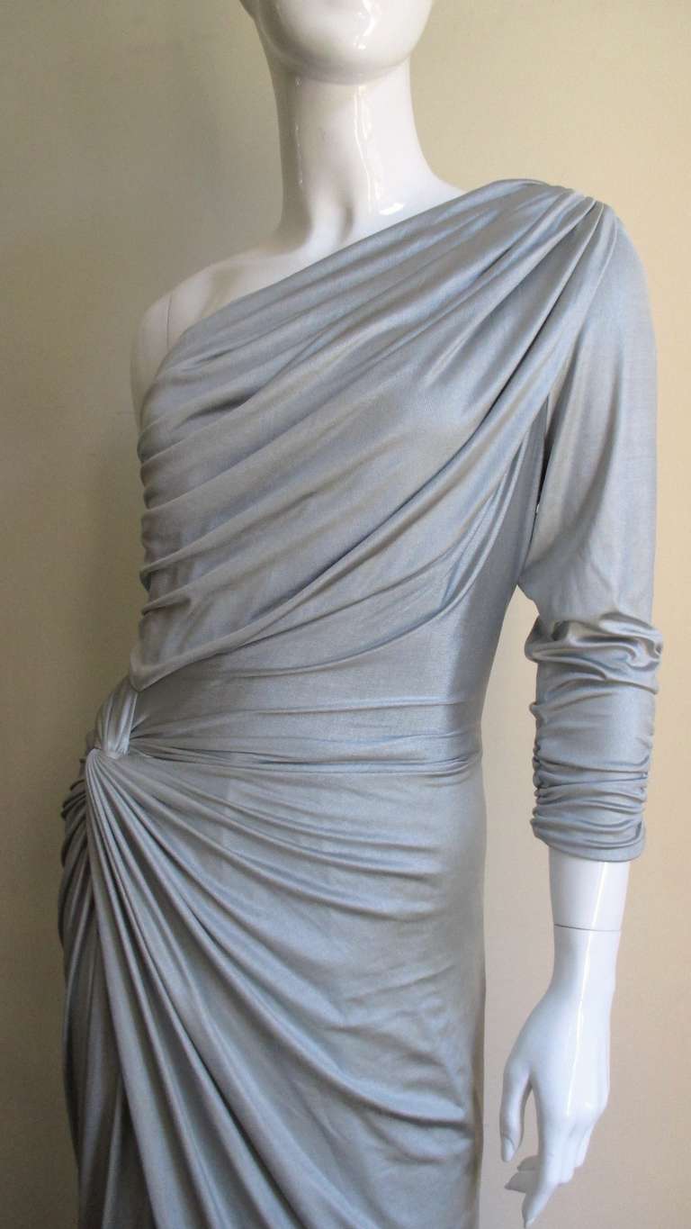 A stunning silver silk knit one shoulder gown from Gianni Versace.  Beautiful draping from one shoulder down to the opposite side (front and back) forming a knot at the hip then crossing and draping down to the hem.  The wrapping of the skirt allows