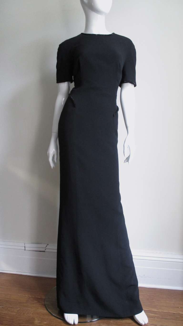 Stunning short sleeved black silk gown from Gianfranco Ferre.  Fitted through the body to knees then a slight flare mermaid style in the front with a sheer gore at the center back hem.  The sleeves are finished in black glass beaded rope as is the