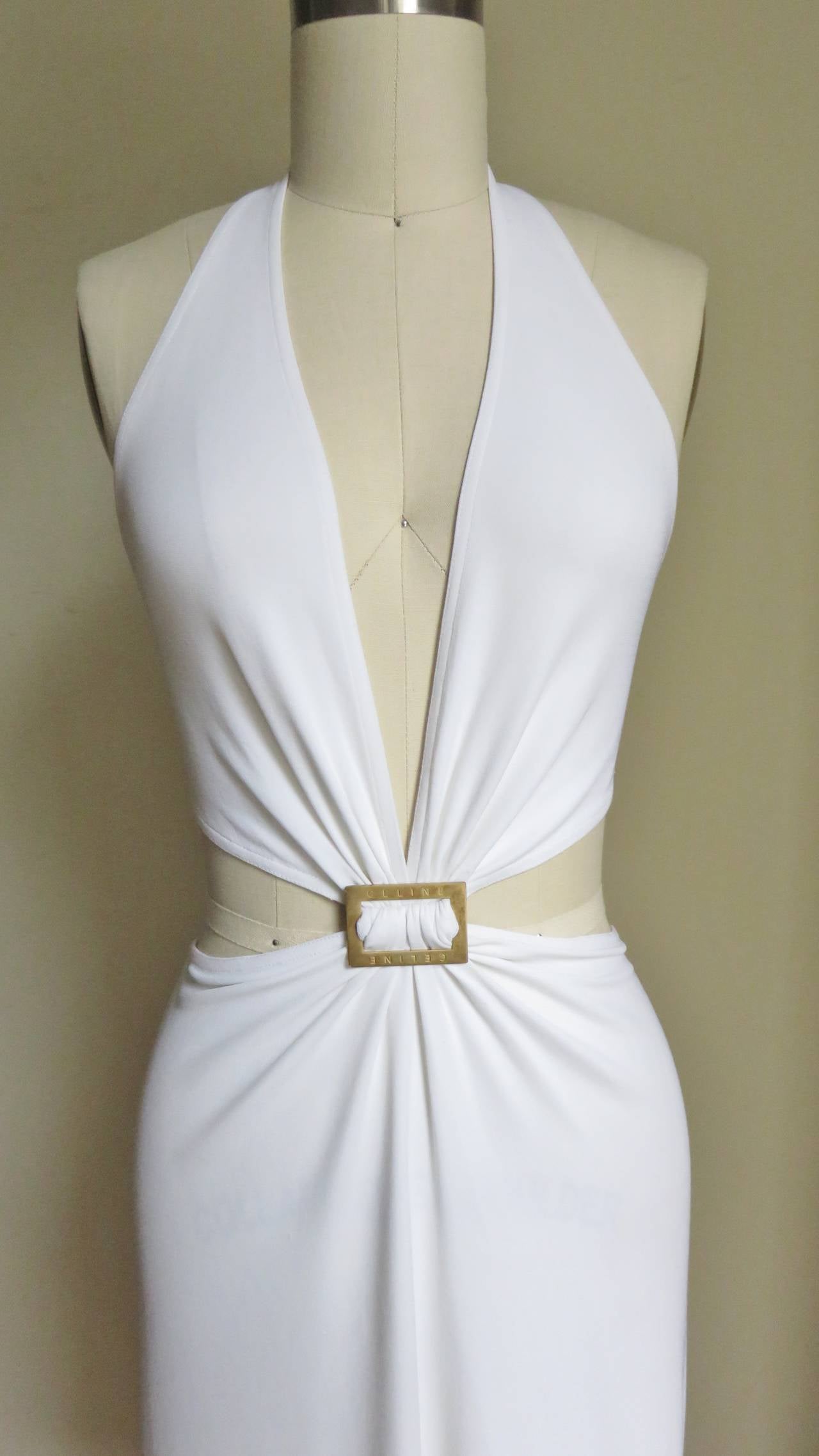 An incredible white silk jersey dress from Celine.  It has a deep plunging halter top which is joined to the skirt only at the center front gathered onto a Celine engraved burnished gold metal rectangle.  The sides are cutout and the back is bare to