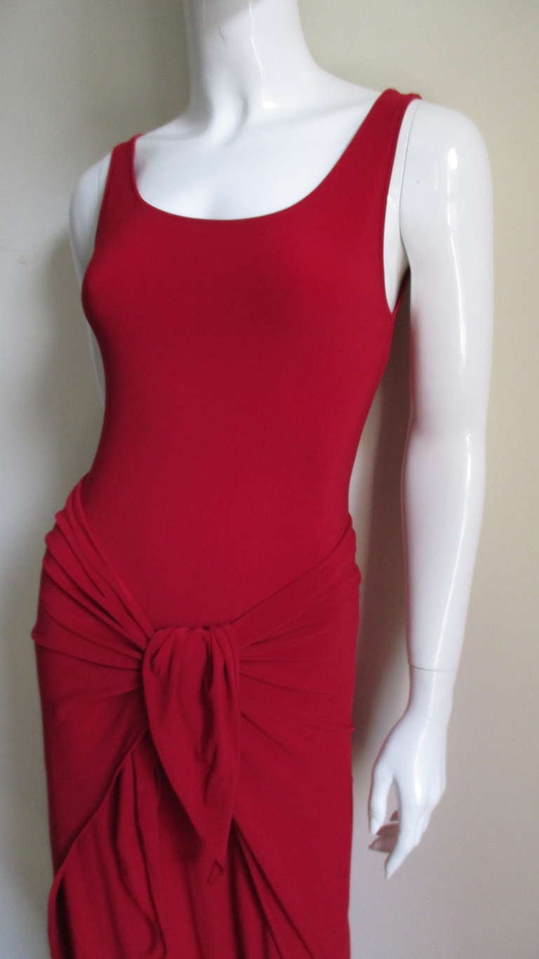 A fabulous unique dress from Norma Kamali in a ruby red silk jersey.  It is sleeveless with a scoop neckline front and back.  It is fitted through the waist and is best described as a low hip length top in back with a front panel that is long enough