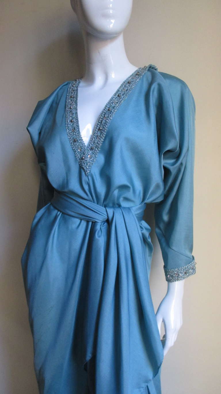 A fabulous teal silk caftan gown from Halston.  It has long dolman sleeves cut in one with the front and back of the dress and a plunging neckline both trimmed with wide braid highlighted with silver threads and rhinestones.  The dress is long and