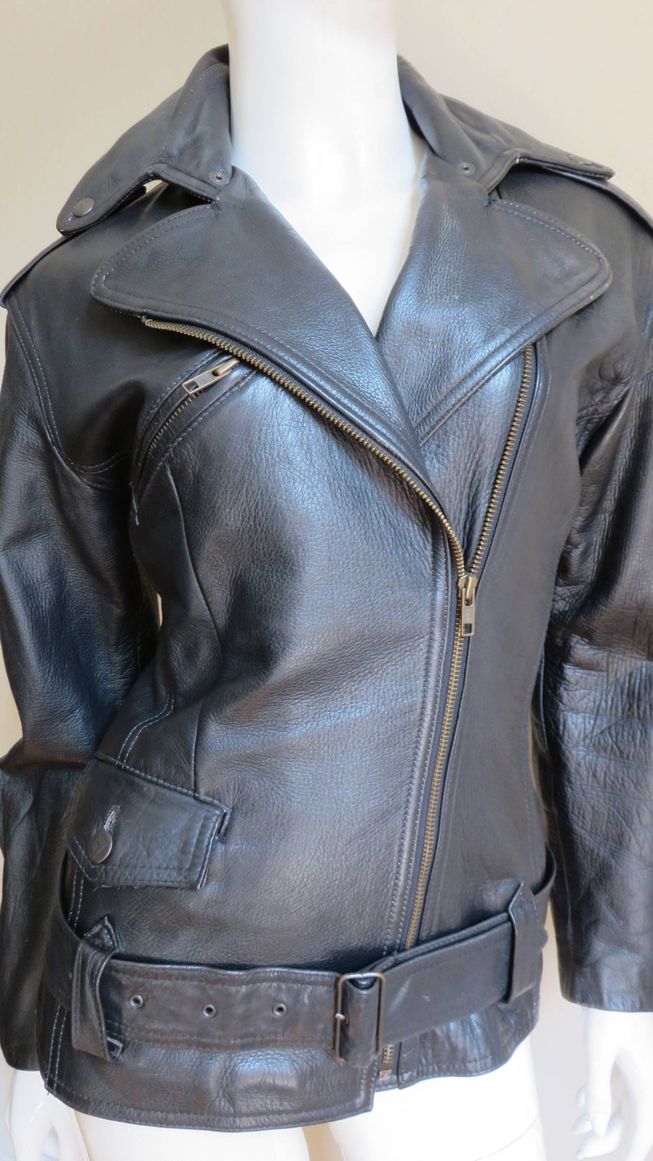 A take on the black motorcycle jacket from Jean Paul Gaultier's Junior Gaultier line.  It is long sleeved with zipper cuffs, a wide lapel collar and epauletts at the shoulders.  There is a zipper breast pocket, a metal Junior Gaultier button on the