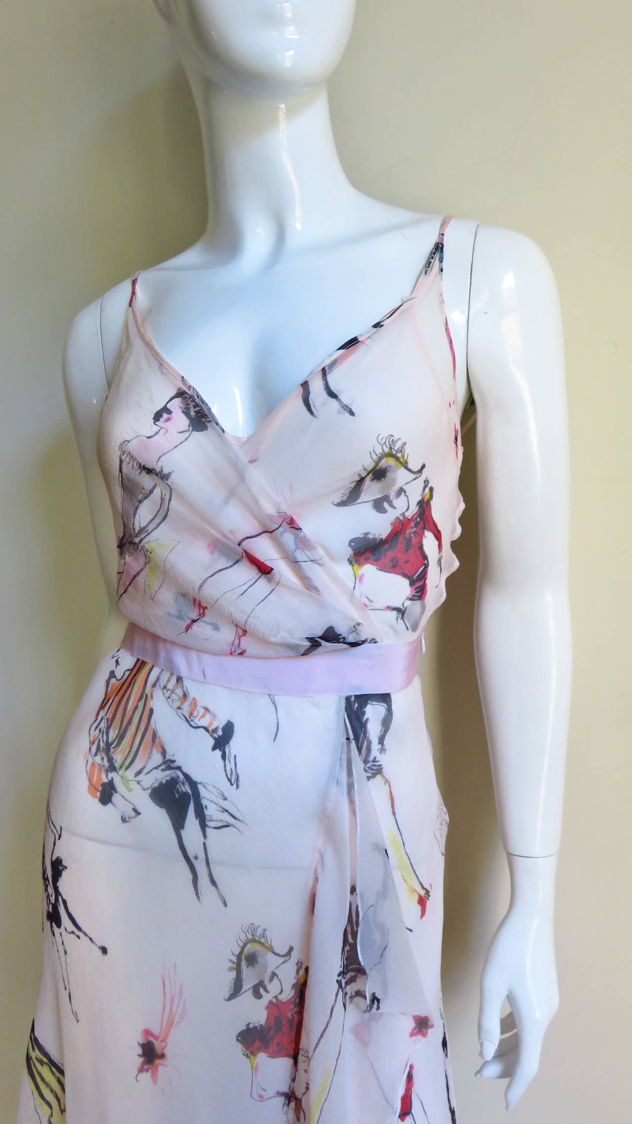 A lovely ethereal dress and matching slip in pale shell pink covered with sketches of people dressed up in costumes drawn in black, red and pink from Moschino.  The slip style dress has a wrap bodice with a matching grosgrain ribbon waist and a