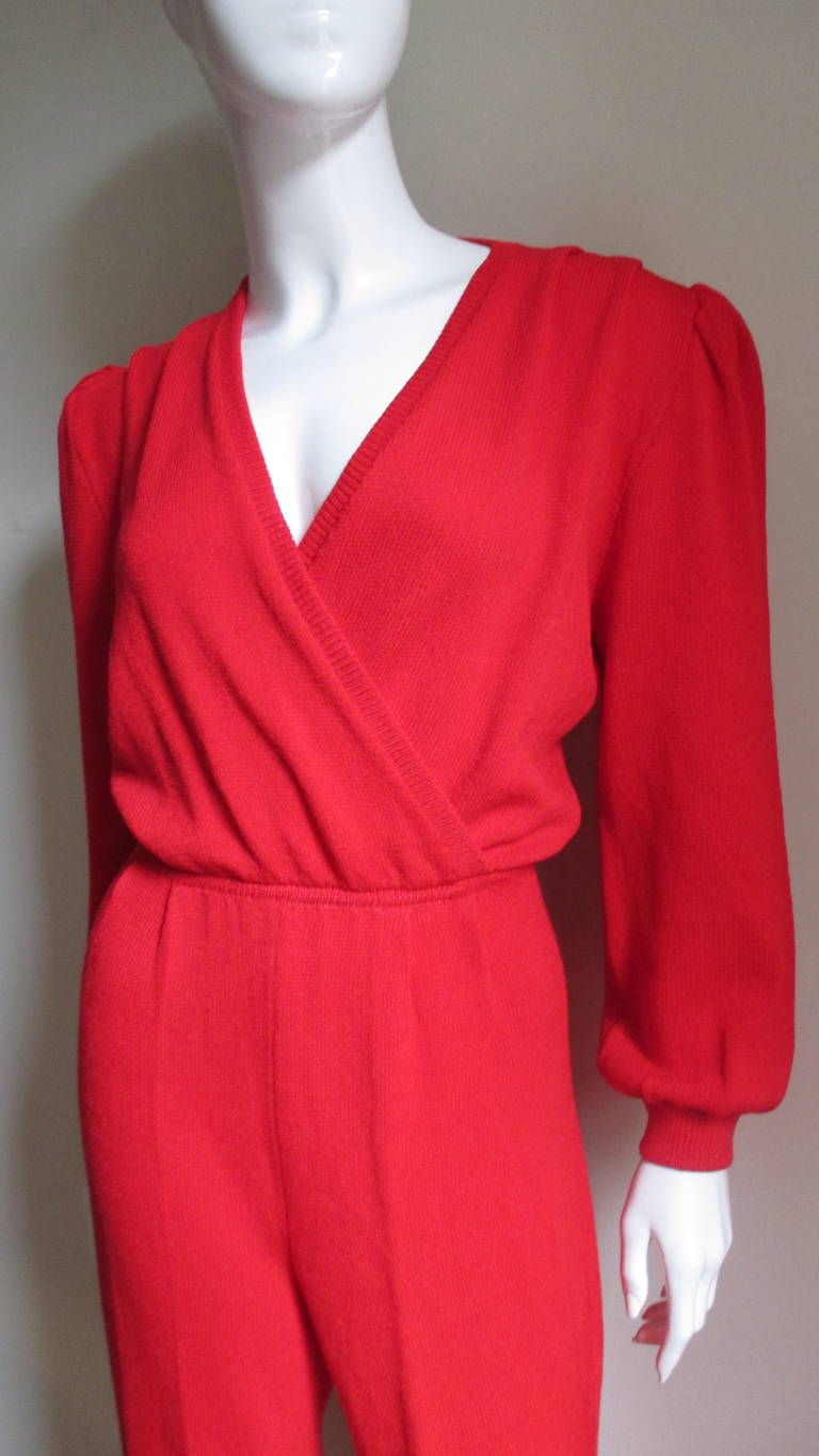 Fabulous wrap jumpsuit from Gianni Versace Couture in red synthetic blend knit.  The bodice wraps in the front creating an adjustable plunge neckline.  There are 4 tiny tucks at the front waistline and shoulders.  The sleeves are  loose with cuffs,