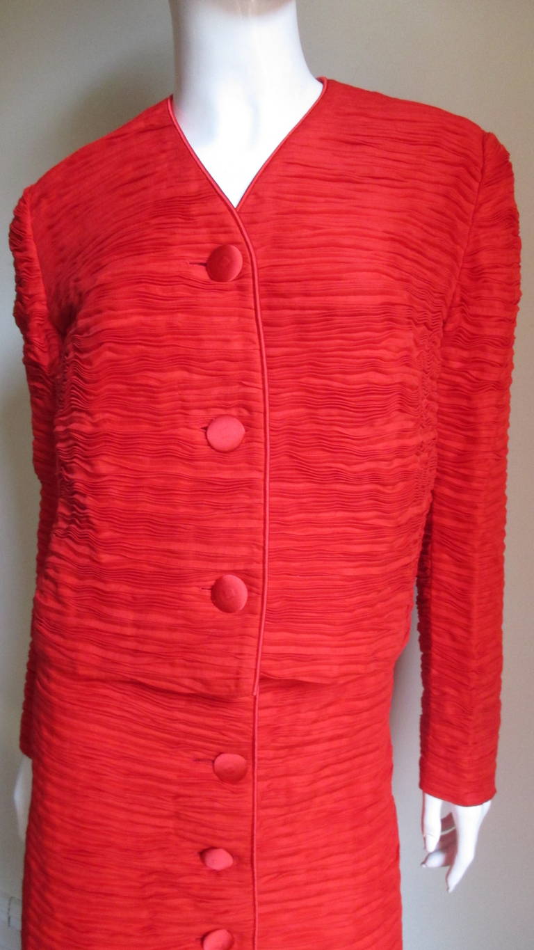 An incredible red suit in delicately pleated fine linen made famous by Sybil Connolly. The jacket closes in front with matching buttons and bound buttonholes. It is piped around the V neckline and along the center front. The A line button front
