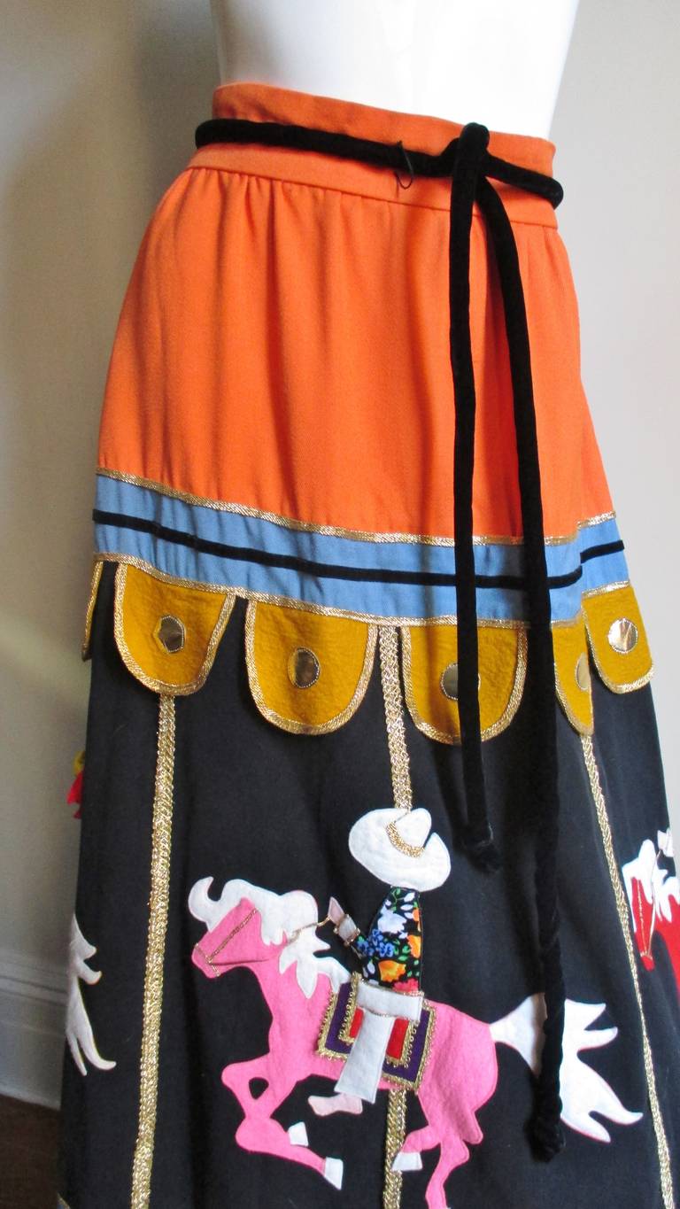 A whimsical, highly detailed skirt from Malcolm Starr in a light weight wool. It is  carousel themed with felt cut-out appliques representing the 4 horses and their riders.  Colorful fabrics are used for the riders' shirts and hair is created with