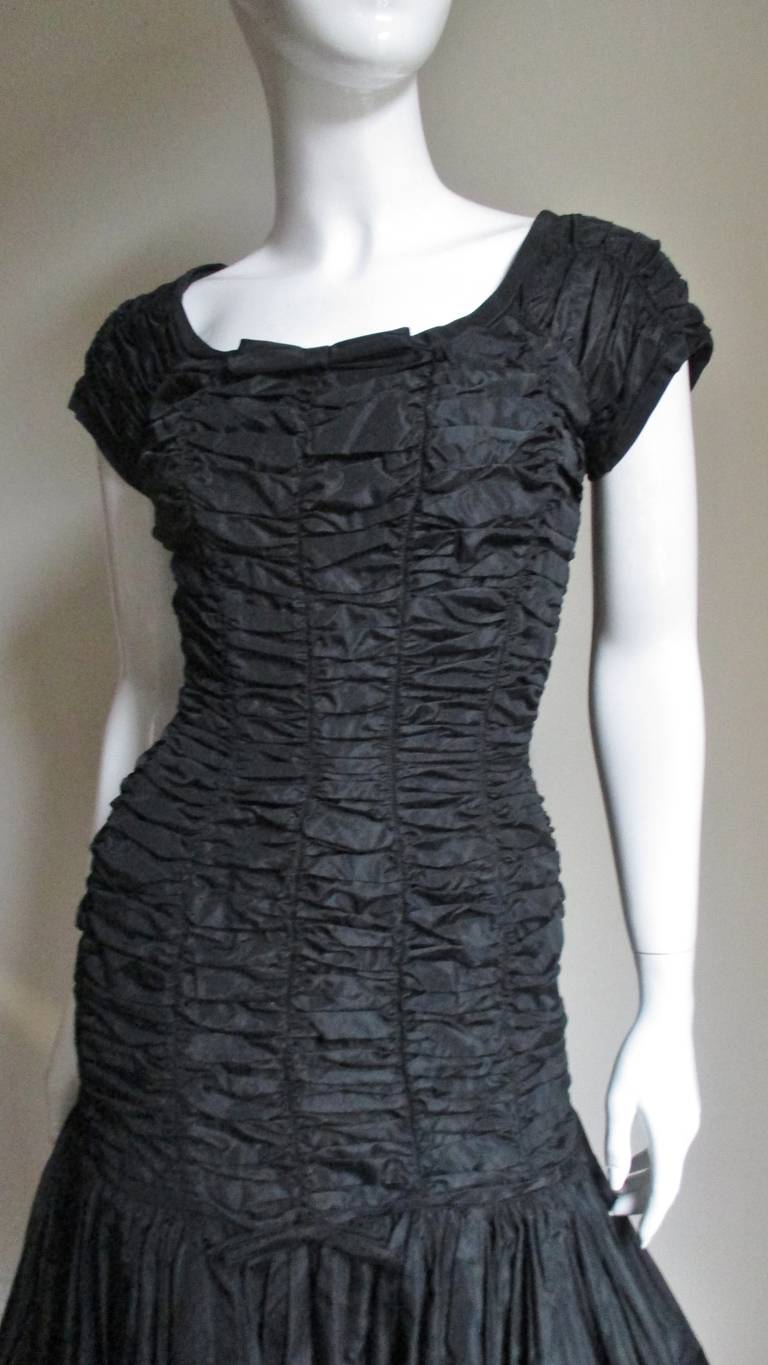Ein fabelhaftes schwarzes Kleid mit Rüschen aus den 1950er Jahren von Suzy Perette.  Es hat einen Rundhalsausschnitt und CAP-Ärmel.  Das Mieder ist halb tailliert und horizontal bis zu den Oberschenkeln gerafft, wo ein geraffter, voller Rock zum