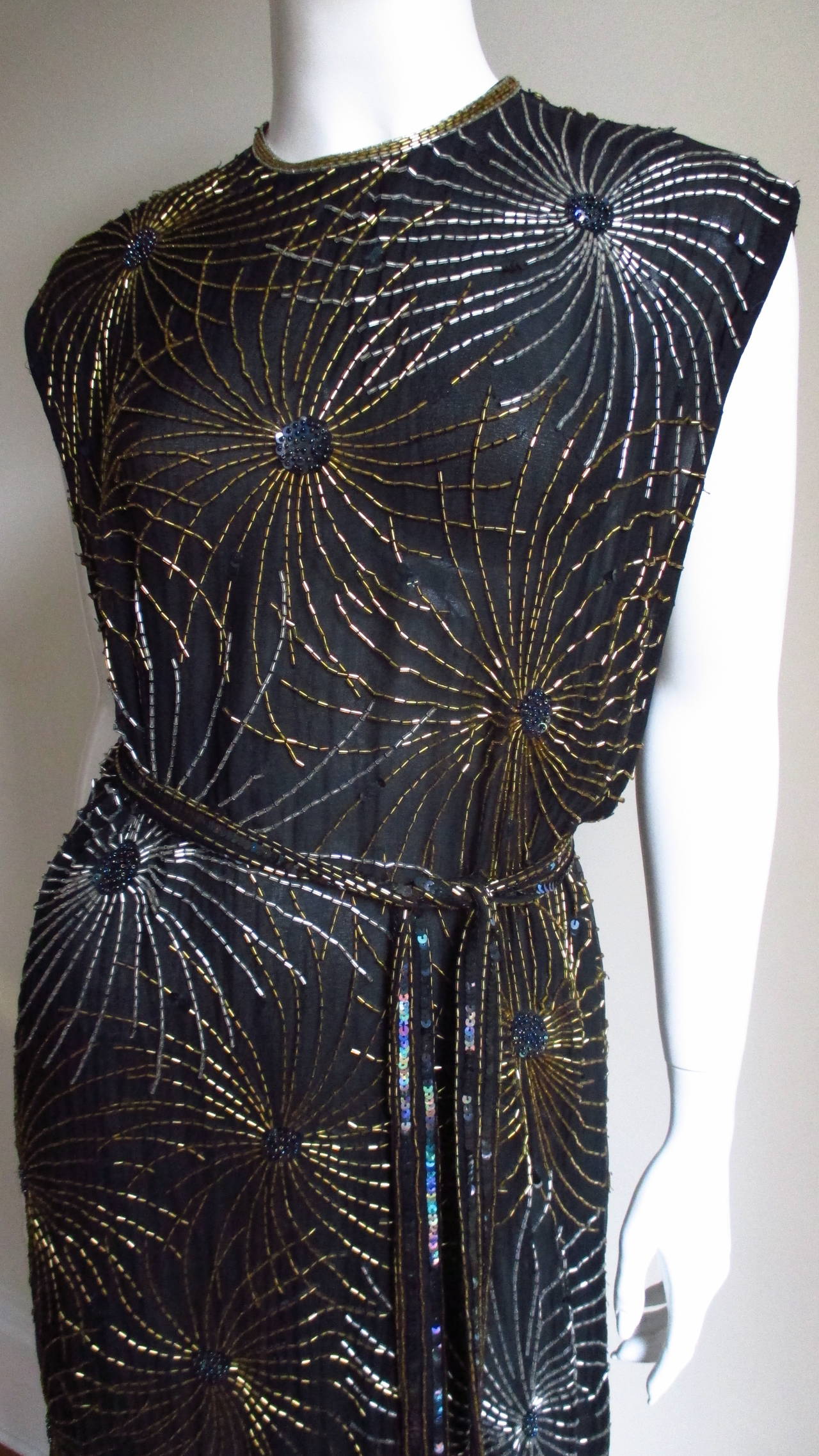 A fabulous black silk dress adorned with sprays of  silver and gold glass tubular beads in a fireworks pattern from Halston lll. It has a simple crew neckline shift with deep cut armholes to the waist exposing the side rib cage and a matching tie