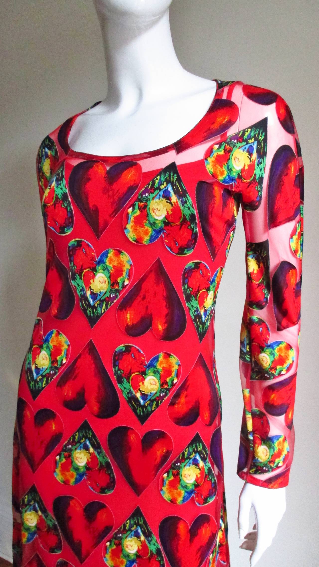A brightly colored dress from Gianni Versace in a synthetic blend.  There are alternating hearts in red and bold colors on a sheer red background.  The dress is long sleeved with a scoop neckline and a 5