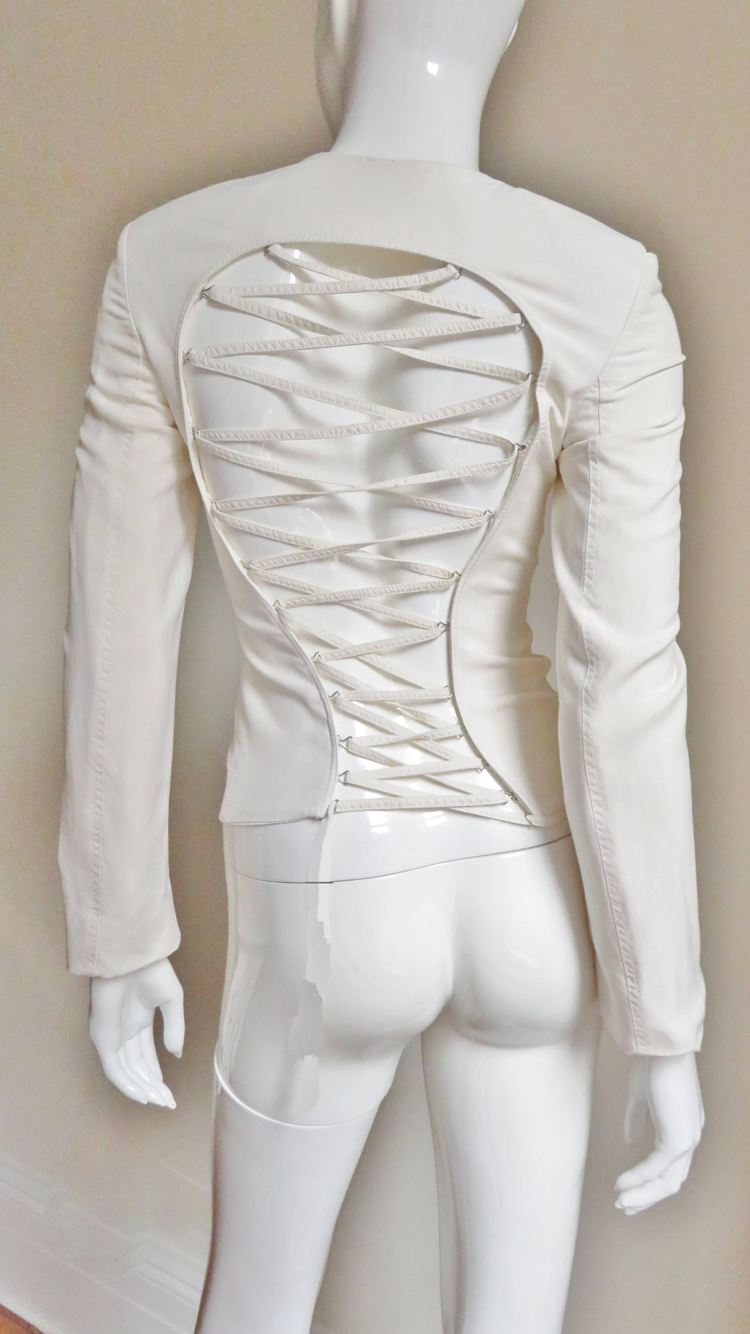 An incredible off white silk jacket from Gianni Versace Couture.  From the front it's a simple fitted, long sleeved, crew neck jacket closing with large hooks and eyes corset style. The back is fabulous with a large cutout to the bottom crisscrossed