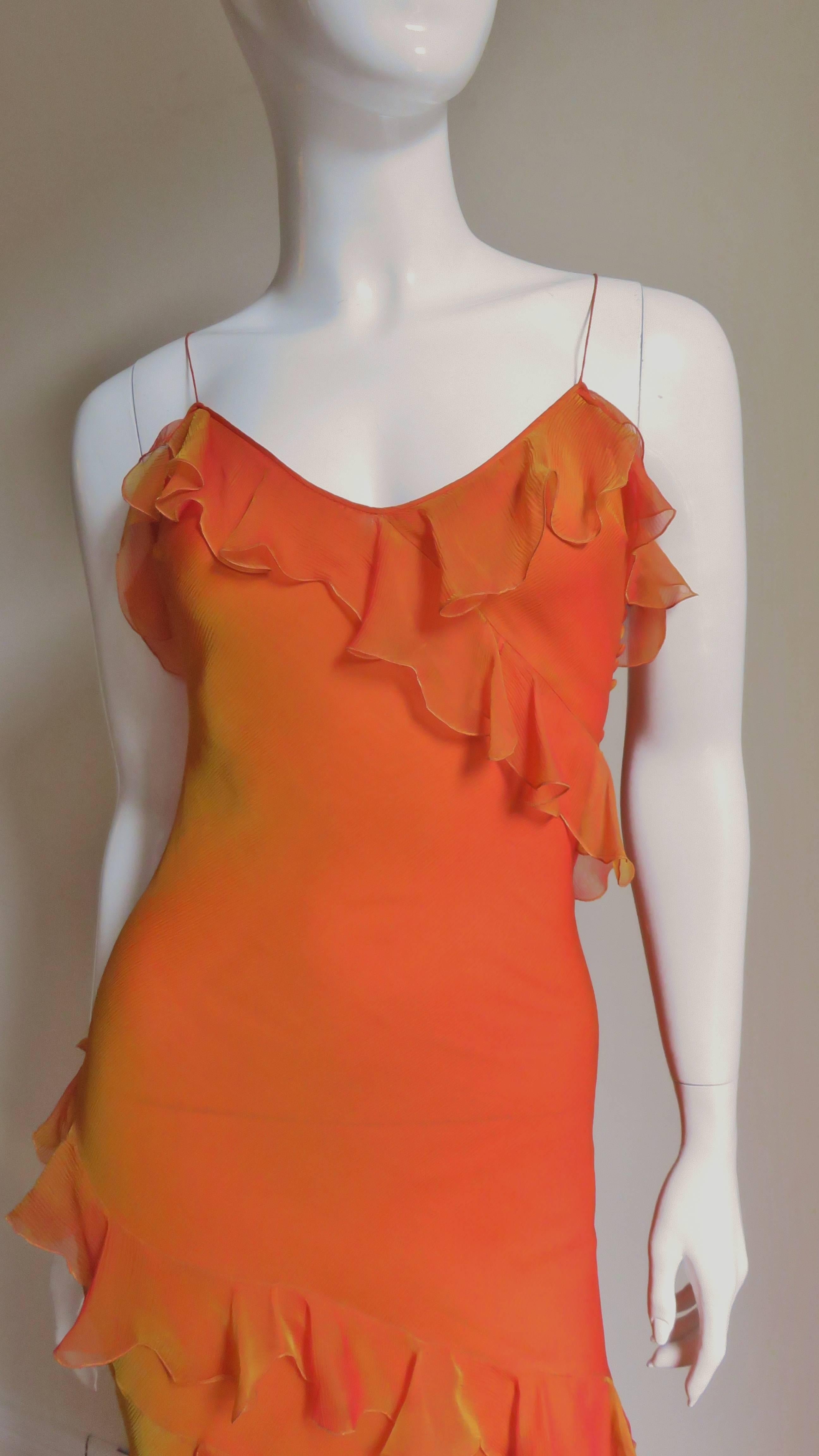 A gorgeous gown in a stunning shade of bright orange with a slight golden iridescence in the light.  It has spaghetti straps, is fitted through the thighs and is adorned with diagonal ruffles around the bodice and at the upper leg at angles.  It has