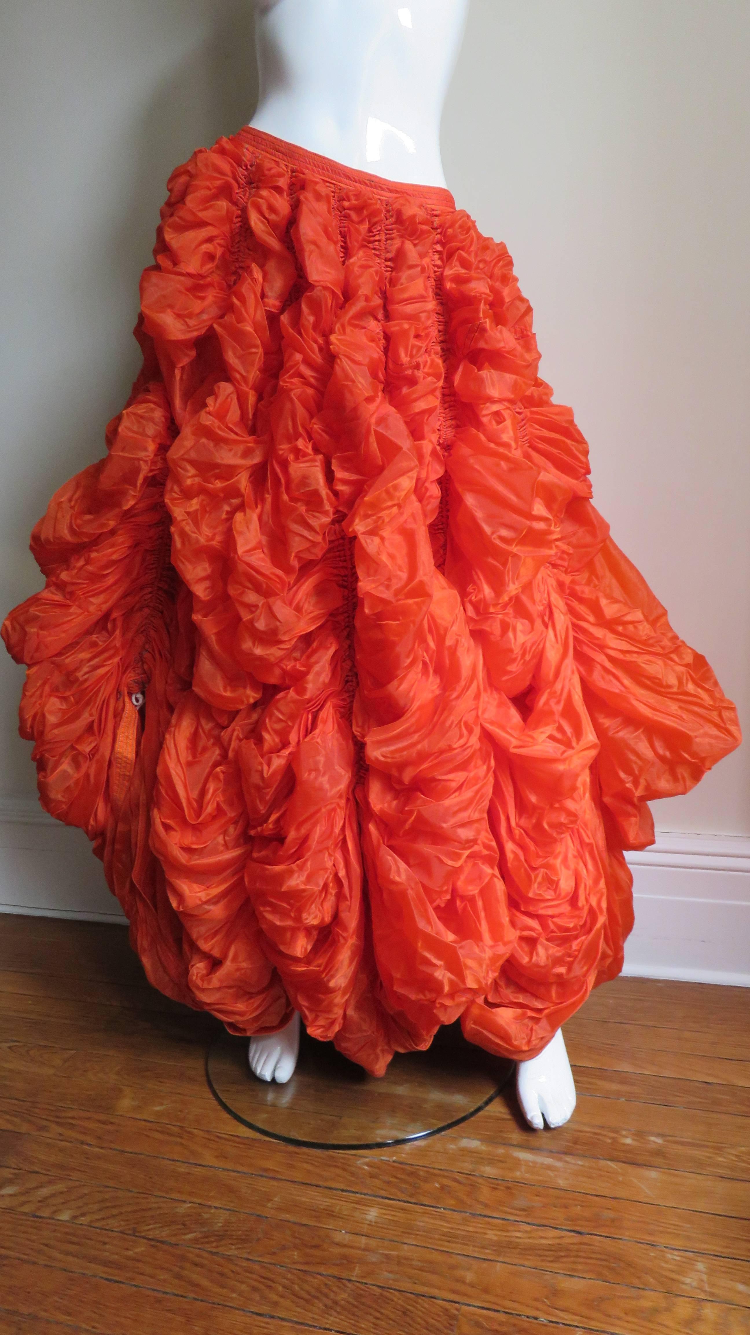 A rare item from Norma Kamali's noteworthy early OMO collection - a tangerine parachute skirt- one was exhibited at the MET in New York. Massive amounts of orange nylon with vertical lines of stitching containing white cord drawstrings around the