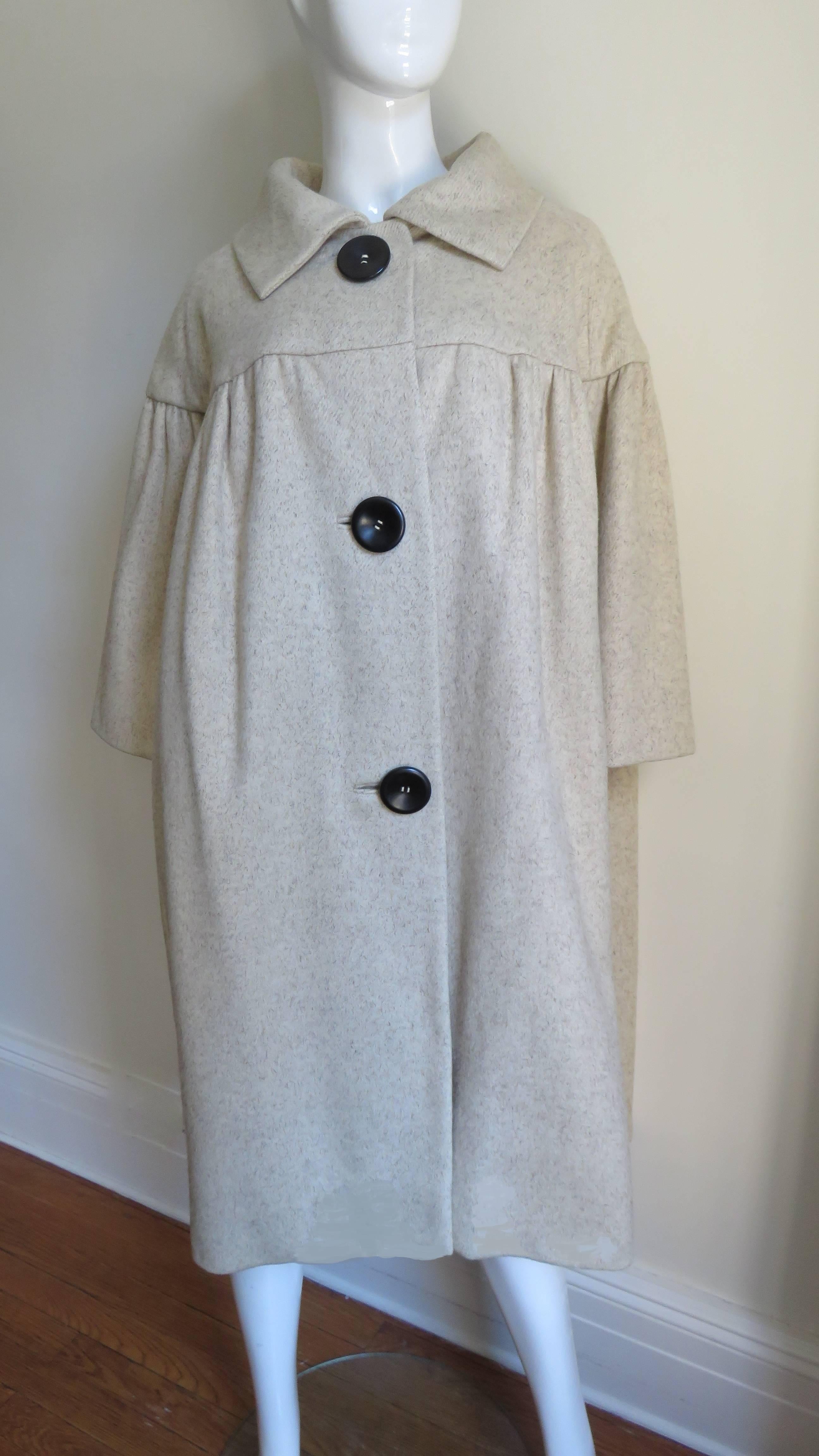 A camel hair coat created by Norman Norell the designer behind the collaboration of Traina-Norell label. The 5 panel body of the coat and the 3/4 length sleeves are gathered onto the yoke front, and back.  There are 3 front bound buttonholes with 3