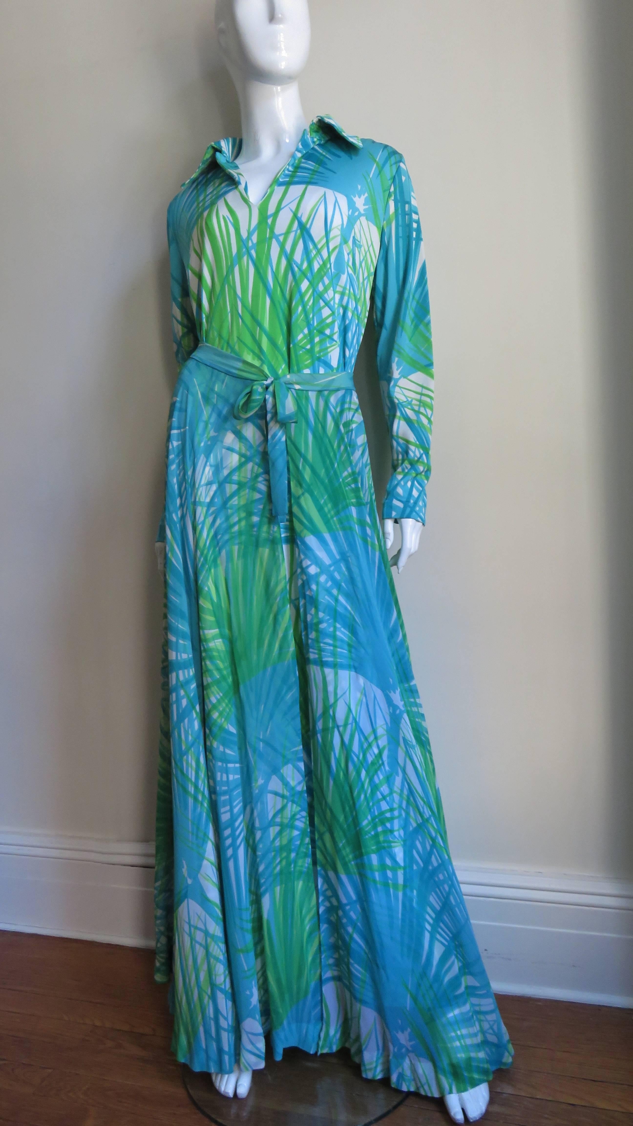 A three piece set from La Mendola, Italy consisting of a long dress, a tie belt and a matching silk over skirt. The pattern is an abstract long grass pattern in shades of blues and greens on synthetic jersey.  The dress has a V neck with a