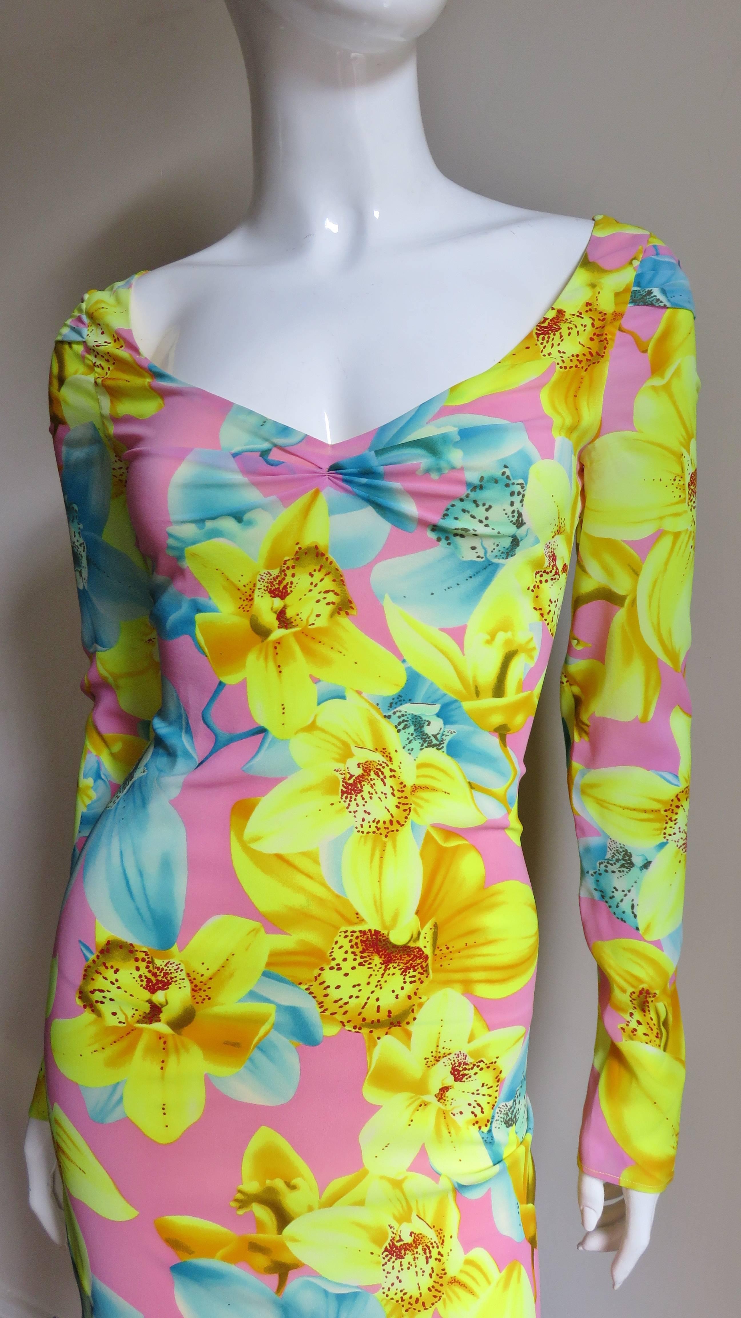 A beautiful fine silk knit dress from Versace in bright yellow, orange and turquoise flowers on a pink background.  It has long sleeves and is fitted with a front and back scoop neckline.  The front neckline has slight center gathering, the back has