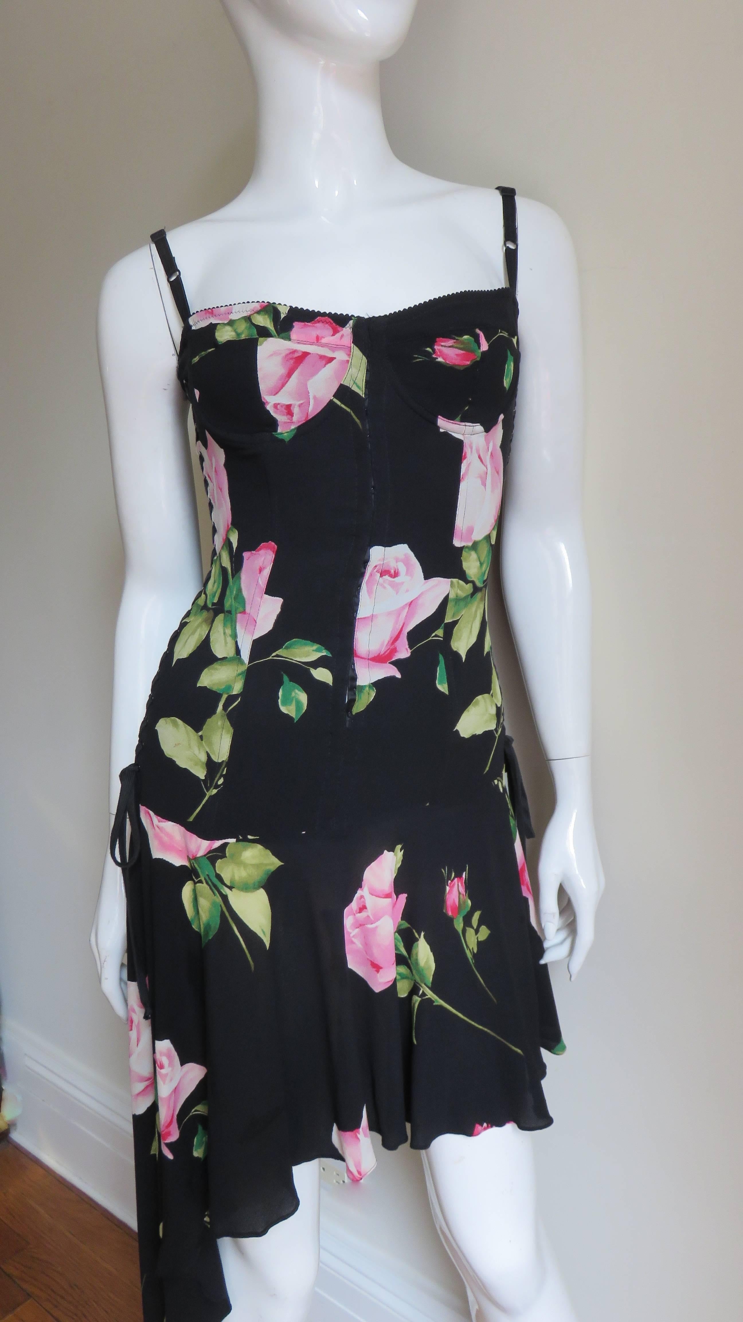 A beautiful pink roses on a black background stretch silk dress by Dolce & Gabbana.  It has an inner fitted, boned, hip length bodice with functional lacing along both sides attaching to an asymmetrical skirt longer on one side. It has a back
