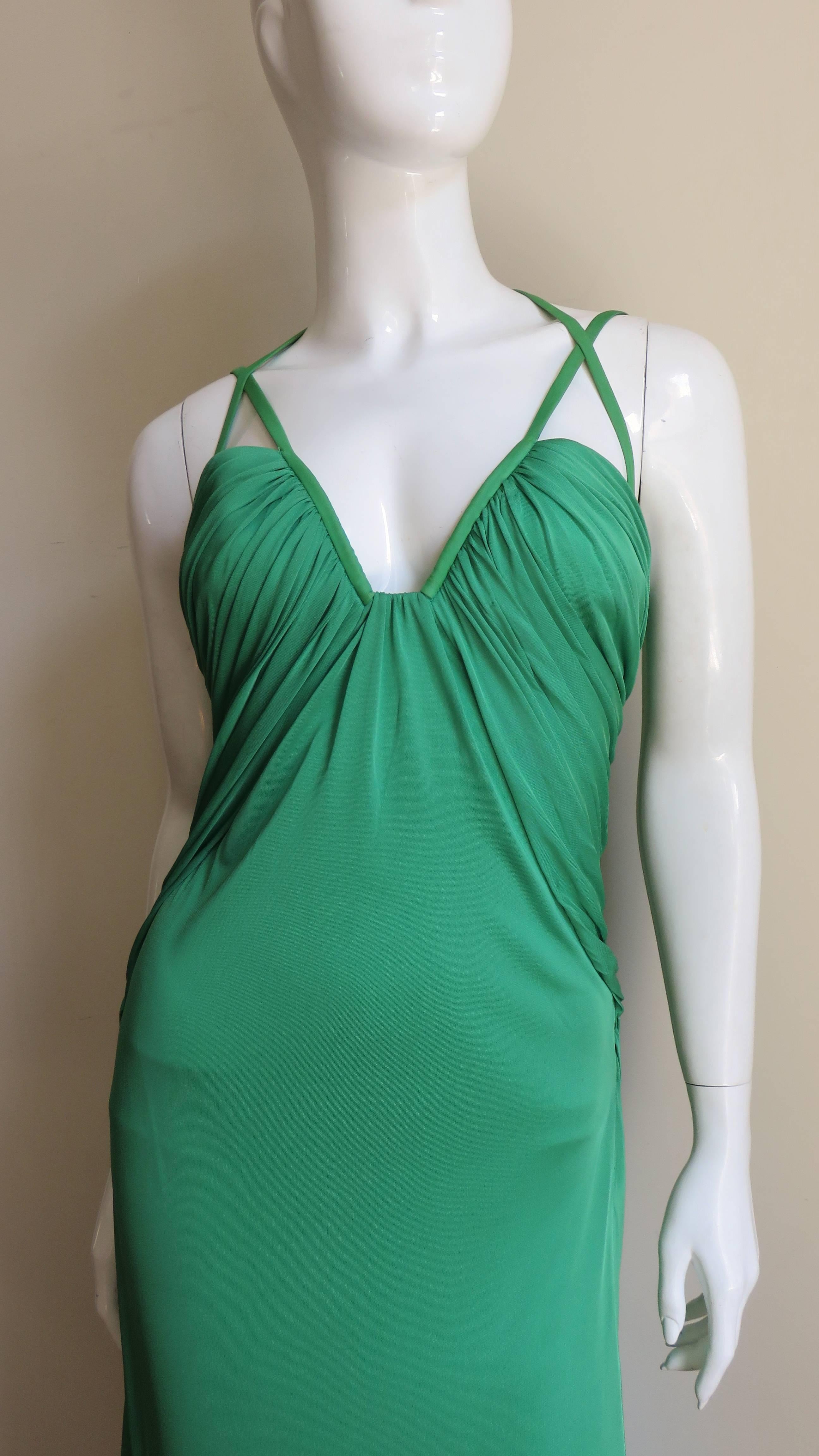 A fabulous gown in emerald green silk knit from Versace.  It has a squared off ruched sweetheart neckline with formed bust cups and piped edges that turn into shoulder straps and a strap that crosses them and goes around the neck.  The bust ruching