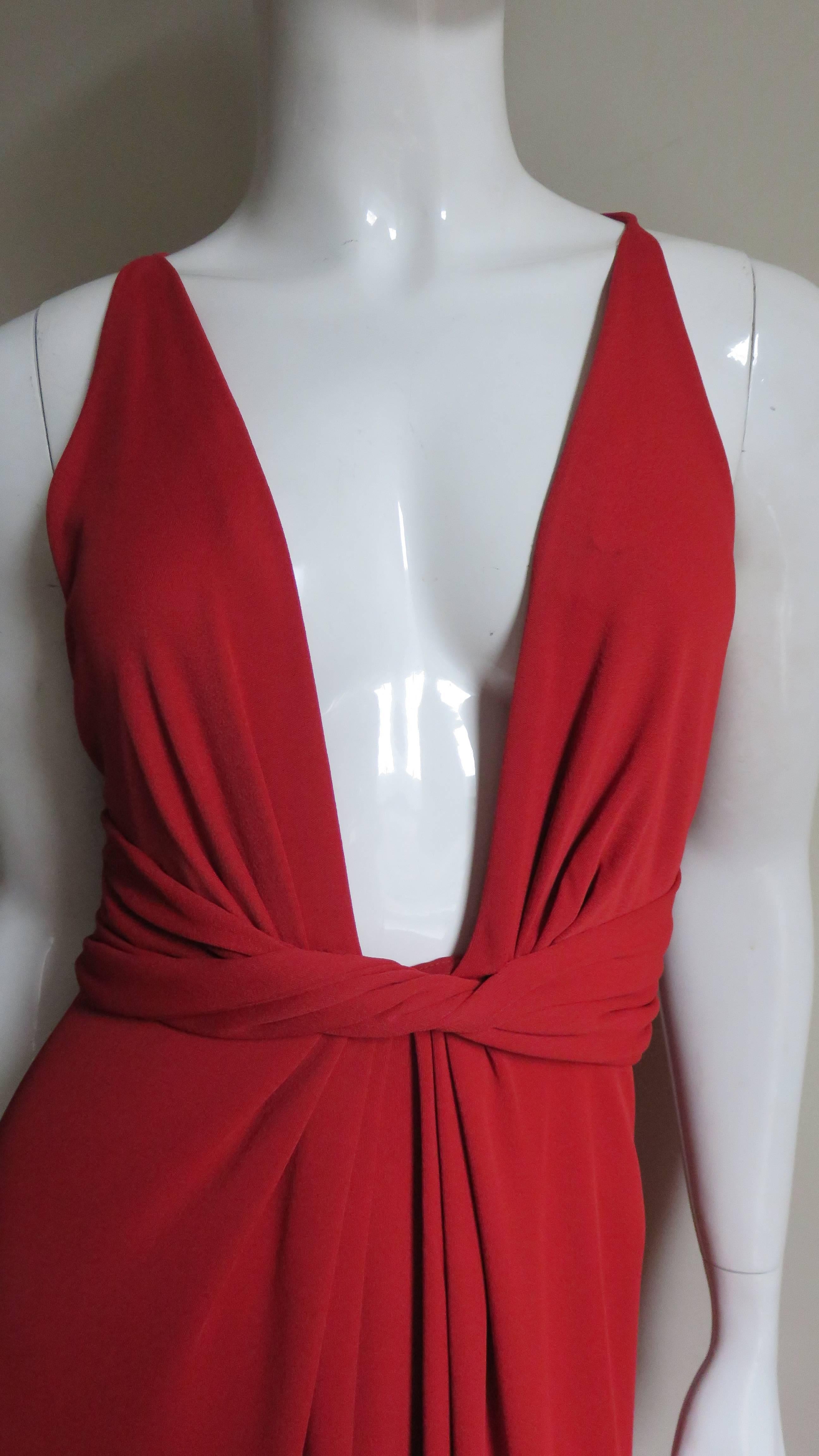 A fabulous rich red jersey gown from Gucci.  It has a plunging front neckline with cut in shoulders and a twisted ruched waist band to accentuate the waist.  The straight skirt has center front fullness at the waist and a slit at the center back