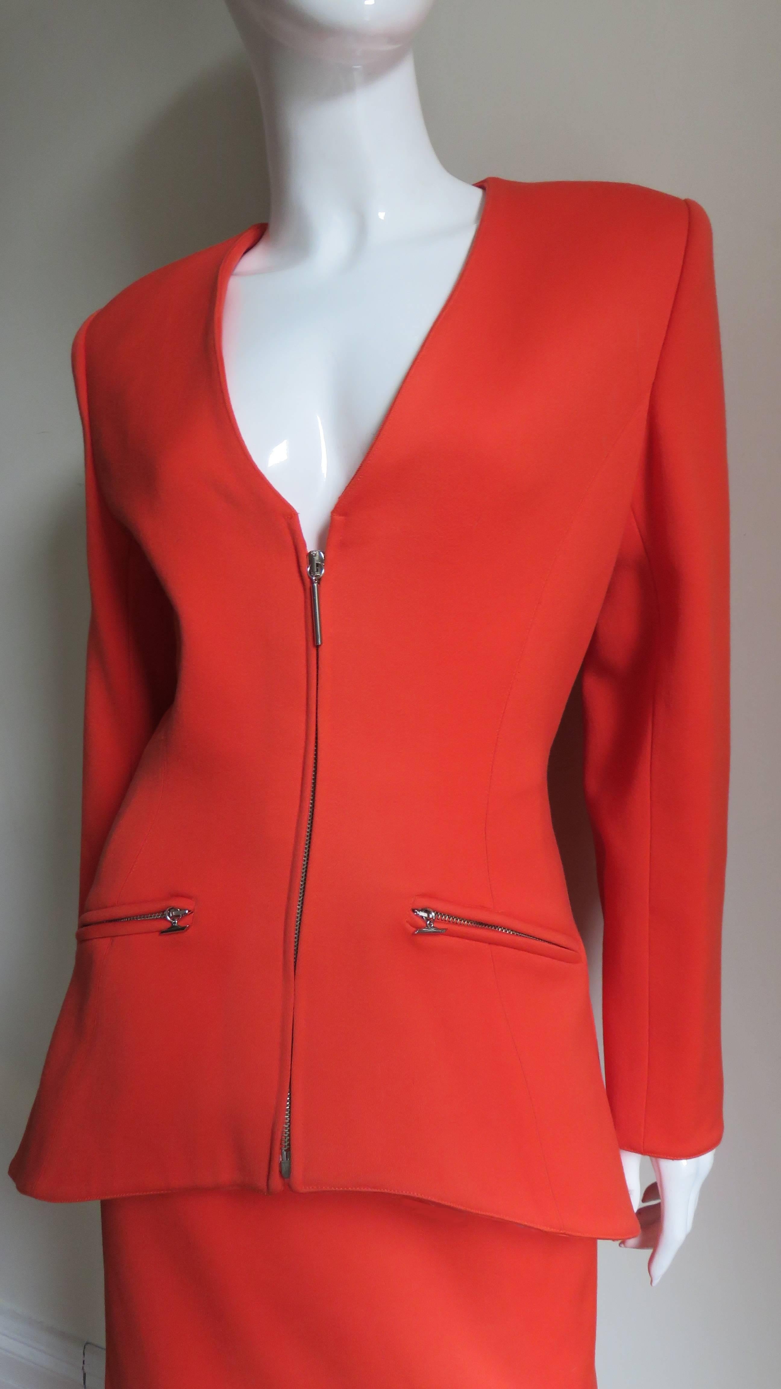 A gorgeous orange wool skirt suit by Claude Montana.  The V neck jacket has vertical seaming creating a great fit.  It closes with a front silver metal zipper, has 3 silver metal rectangular buttons on each cuff and 2 front zipper hip pockets. It is