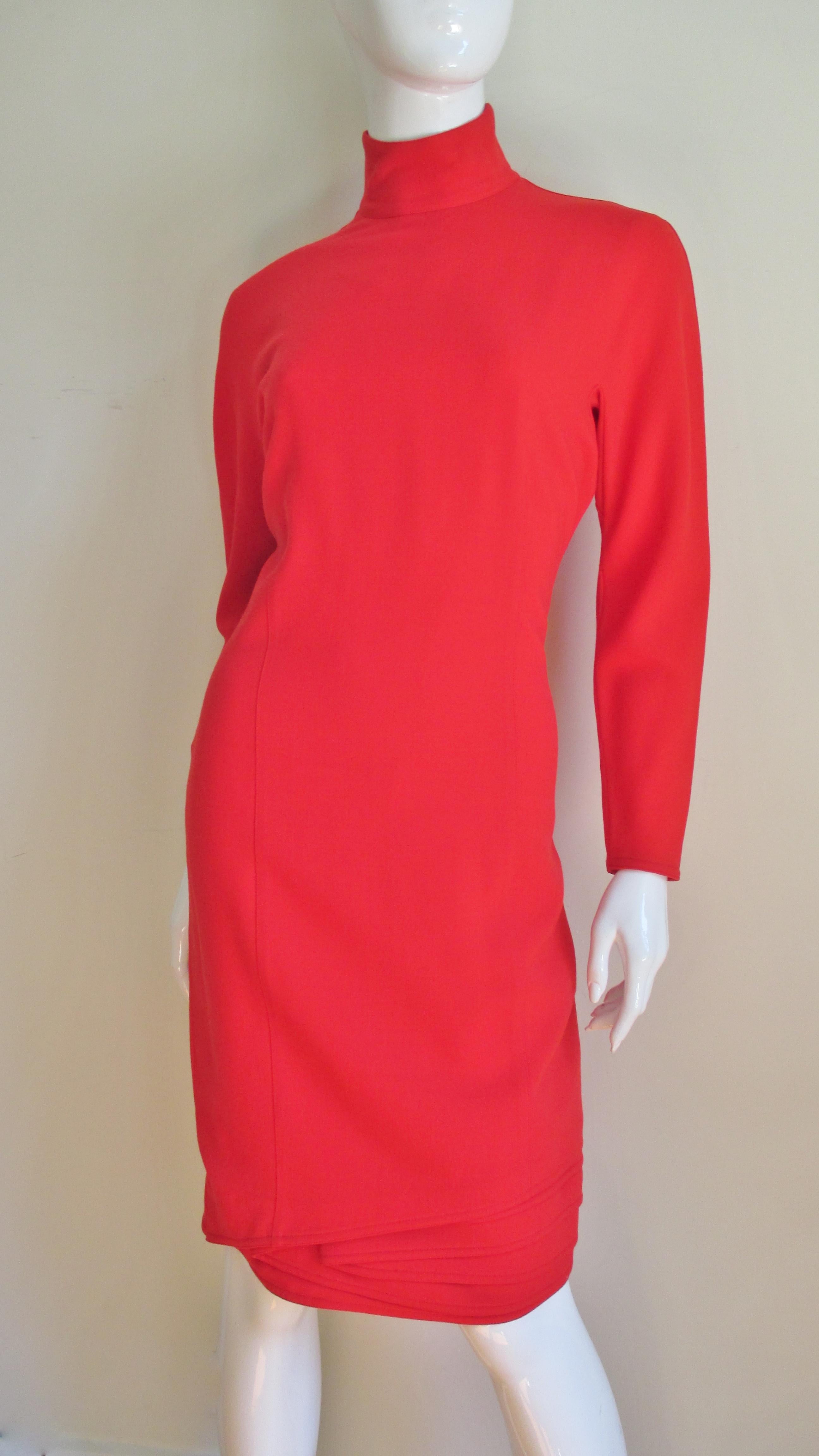 A fabulous lightweight orange wool dress by Gianni Versace.  It is semi fitted with a stand up collar, subtle long dolman sleeves and intricate layers of angled folds at the hemline front and back. it is lined in matching silk and has a center back