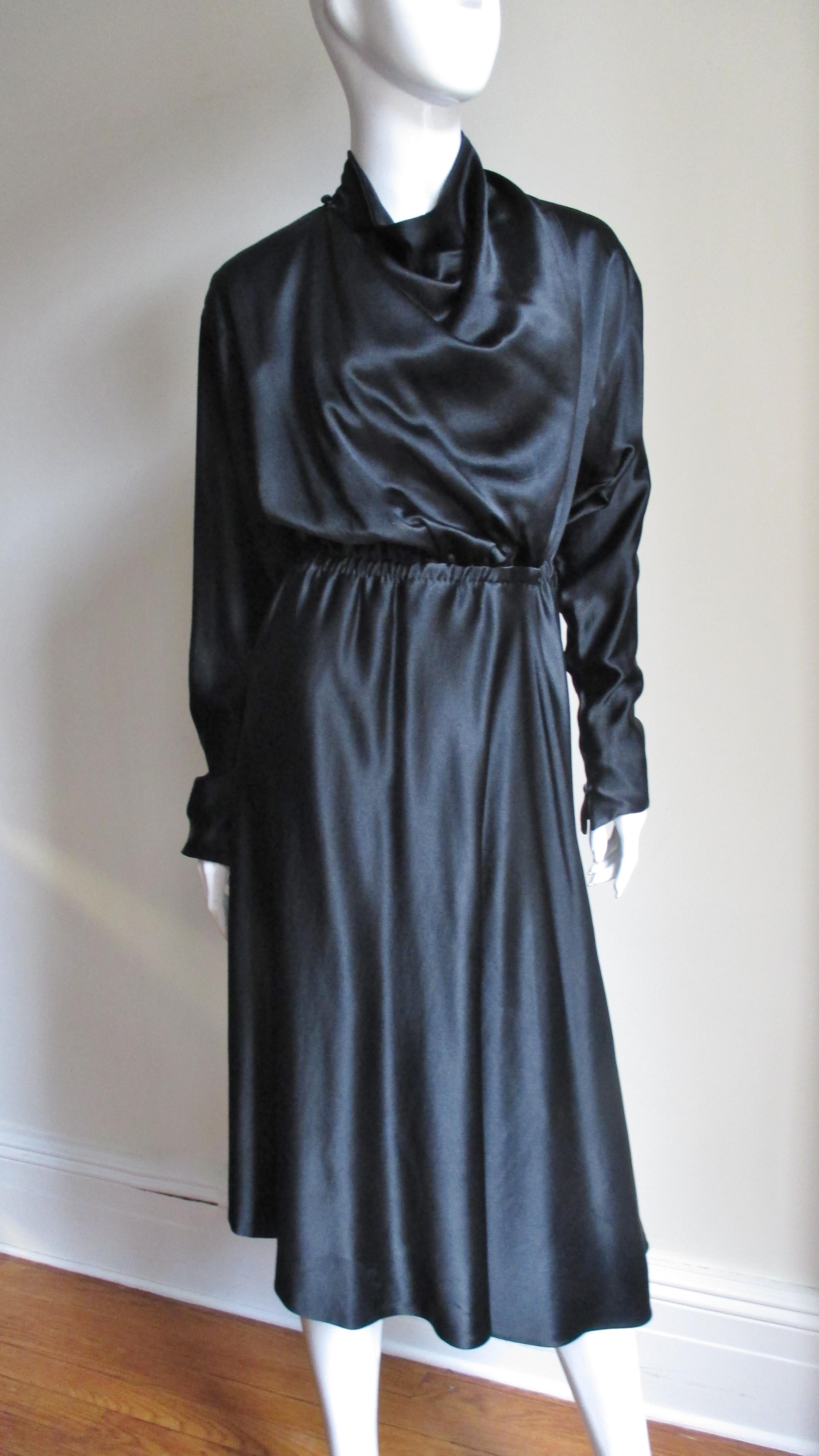 A gorgeous rich black silk wrap dress by Halston. It has a wrap front, draped neckline buttoning at the shoulder and long dolman sleeves with pointed button cuffs. The waist is gathered and has stretch allowing for a flexible, comfortable fit with a