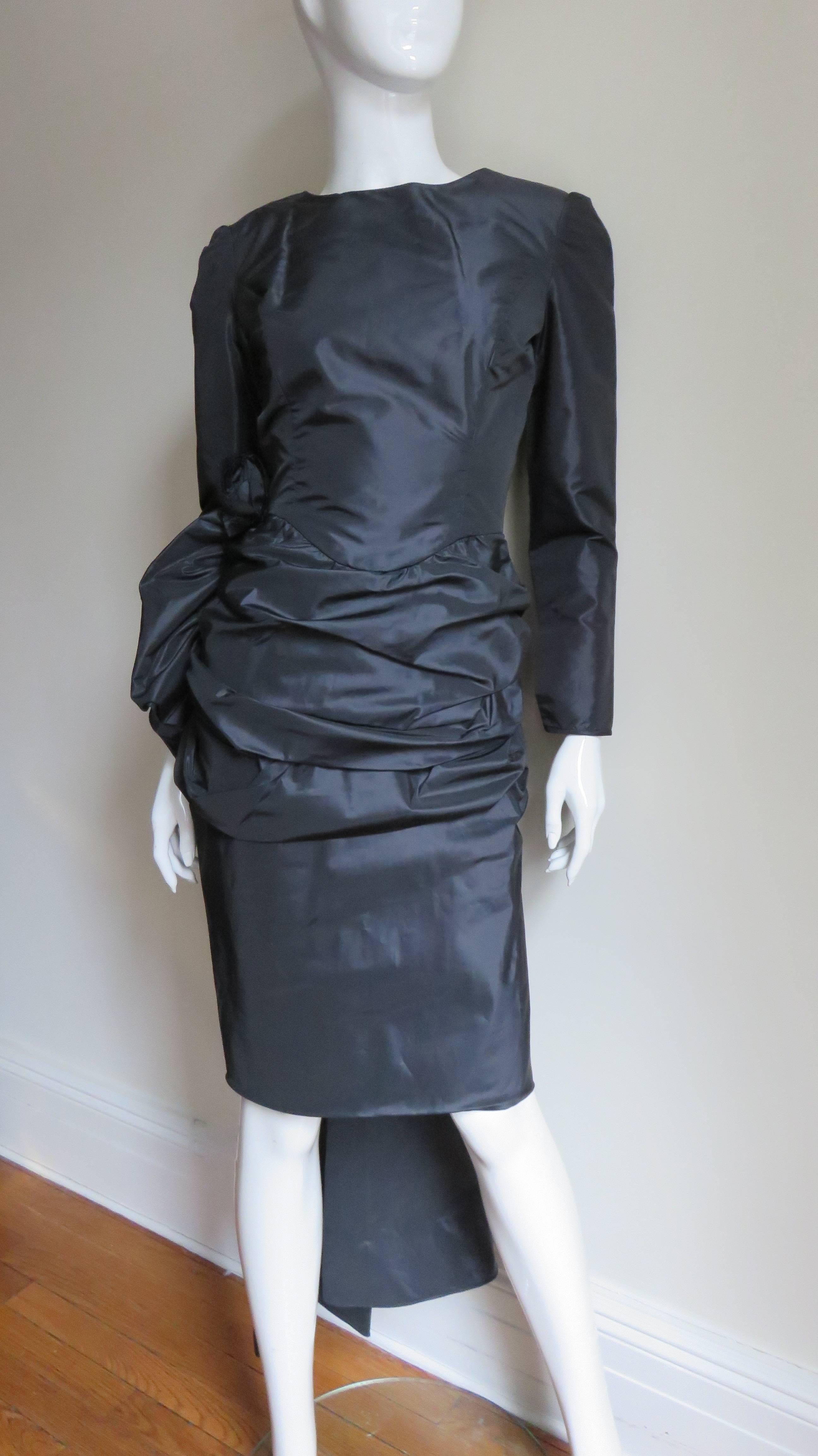 A fabulous black taffeta dress from Victor Costa.  It has a deep V back with an elaborate double drape layer decorated with black appliqued flowers of the same fabric below it and 2 panels emanating from it falling to the calf.  The front is simple