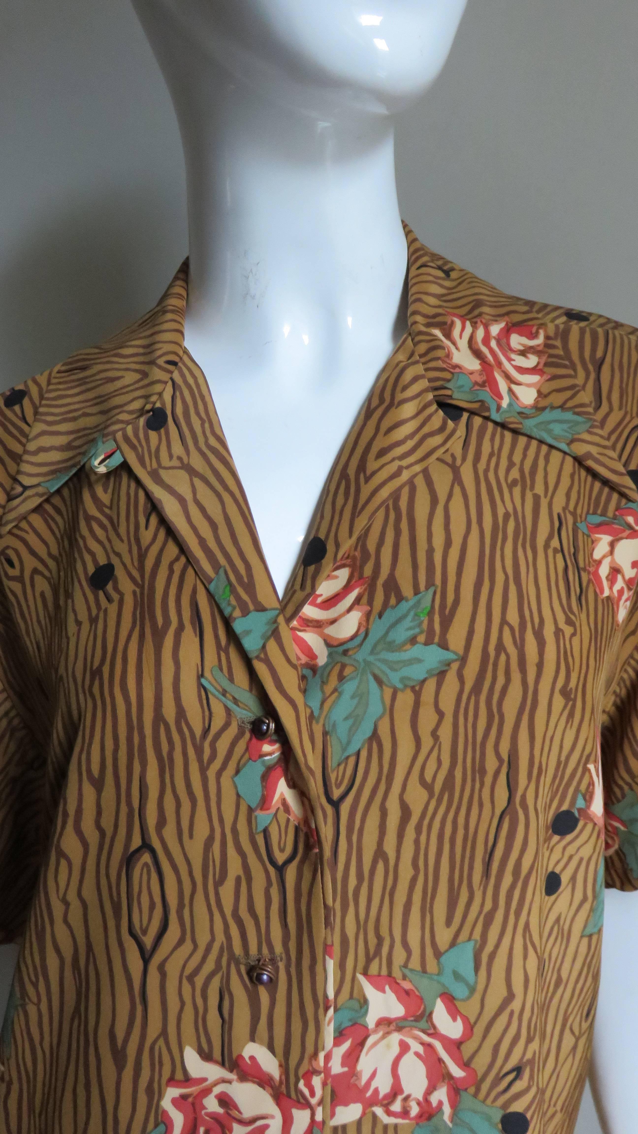 A great silk shirt from Todd Oldham.  It has short sleeves and a shirt collar with copper coiled buttons up the front.  The colors and patterns are signature Todd Oldham consisting of a faux wood grain background with a smattering of orange roses