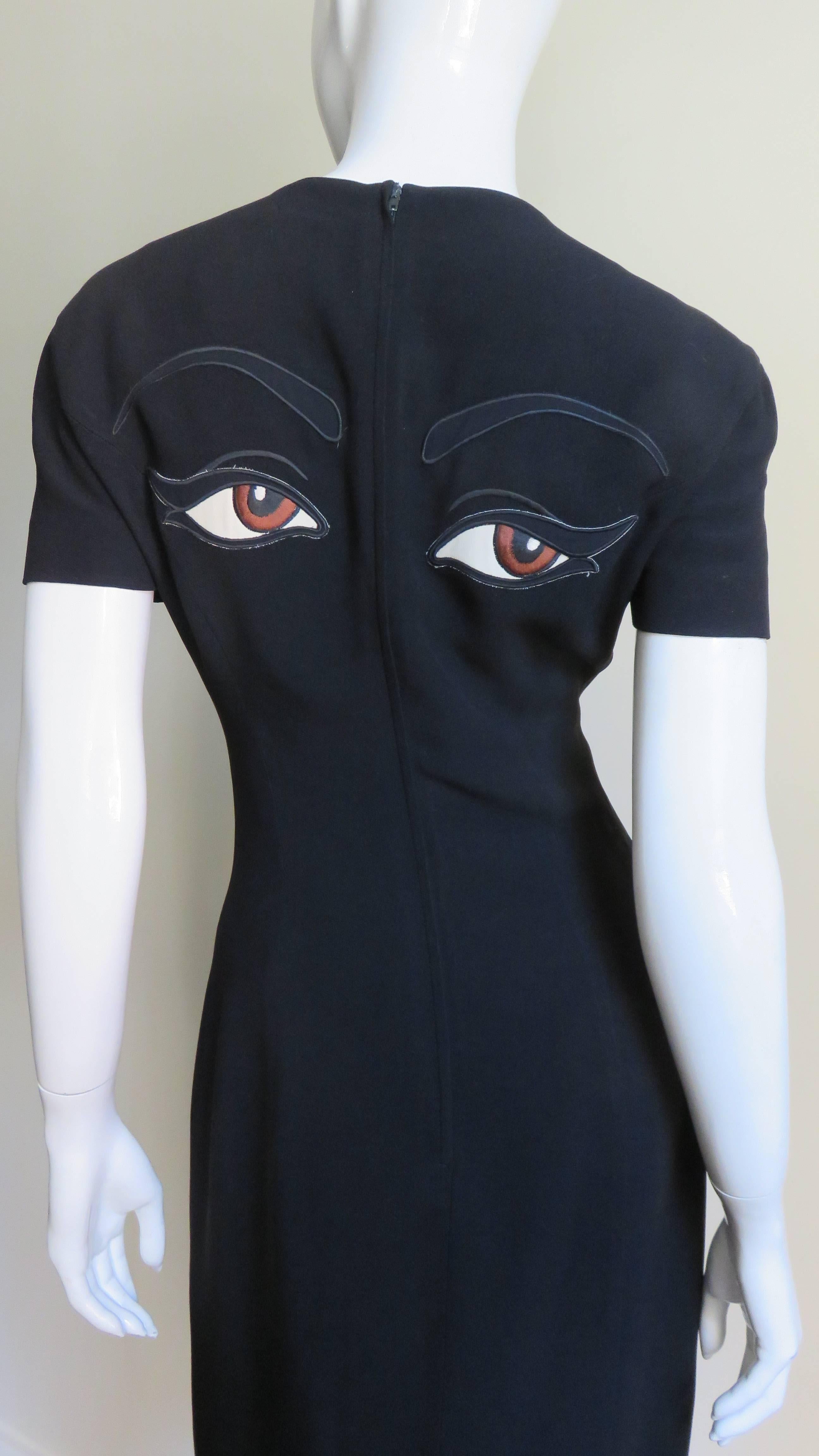 A simple black dress from Moschino Couture with a twist.  It has short sleeves, a crew neck and is semi fitted with princess seams . There are a pair of large brown embroidered eyes and eyebrows appliqued on the upper back. It is fully lined in