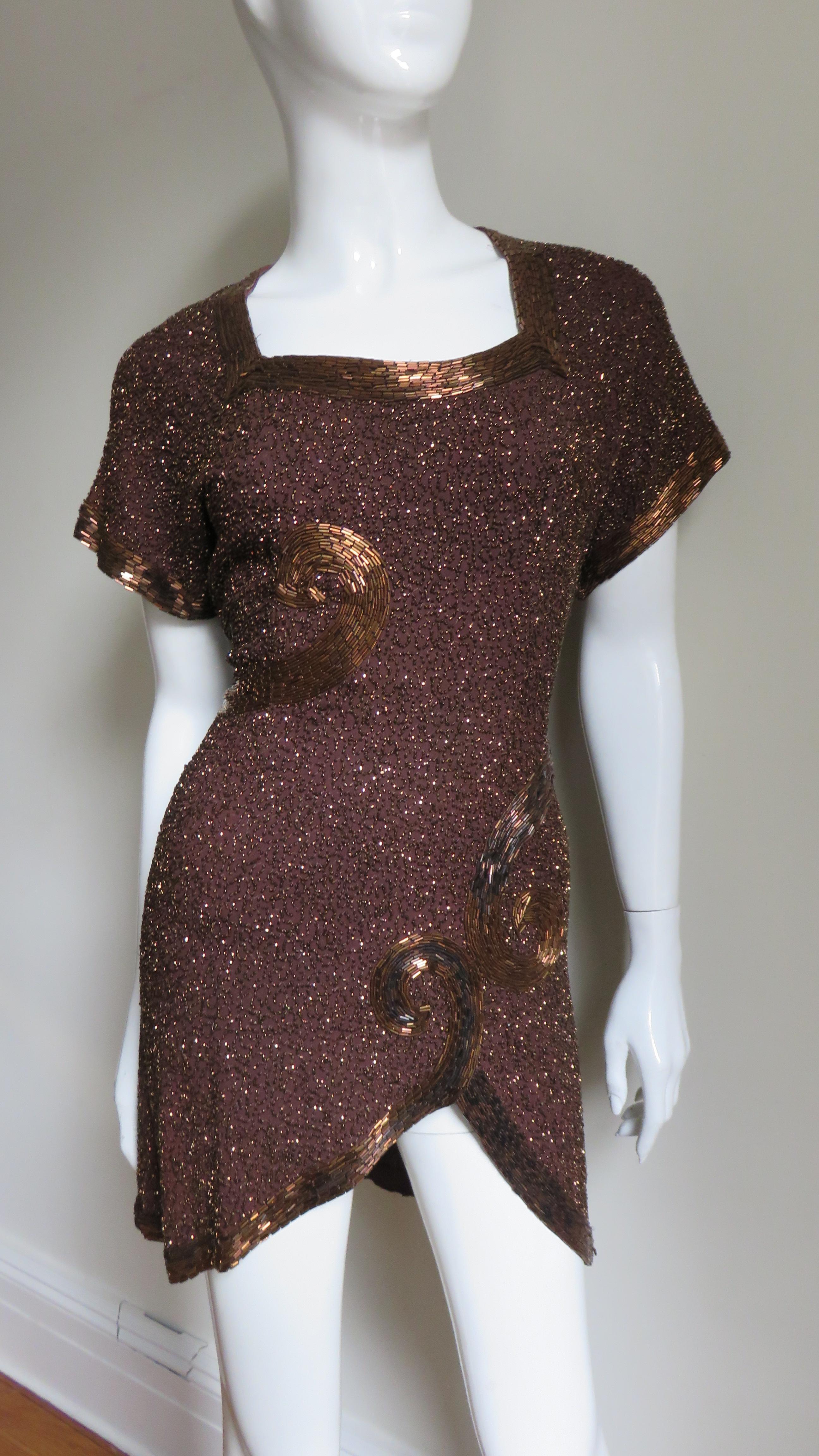 An incredible brown silk top tunic from Wilma New York. It has short dolman sleeves, a square neck and an asymmetric hemline. The sleeves, neckline and hemline have rows of artfully placed matching brown glass tubular beads with a scroll design