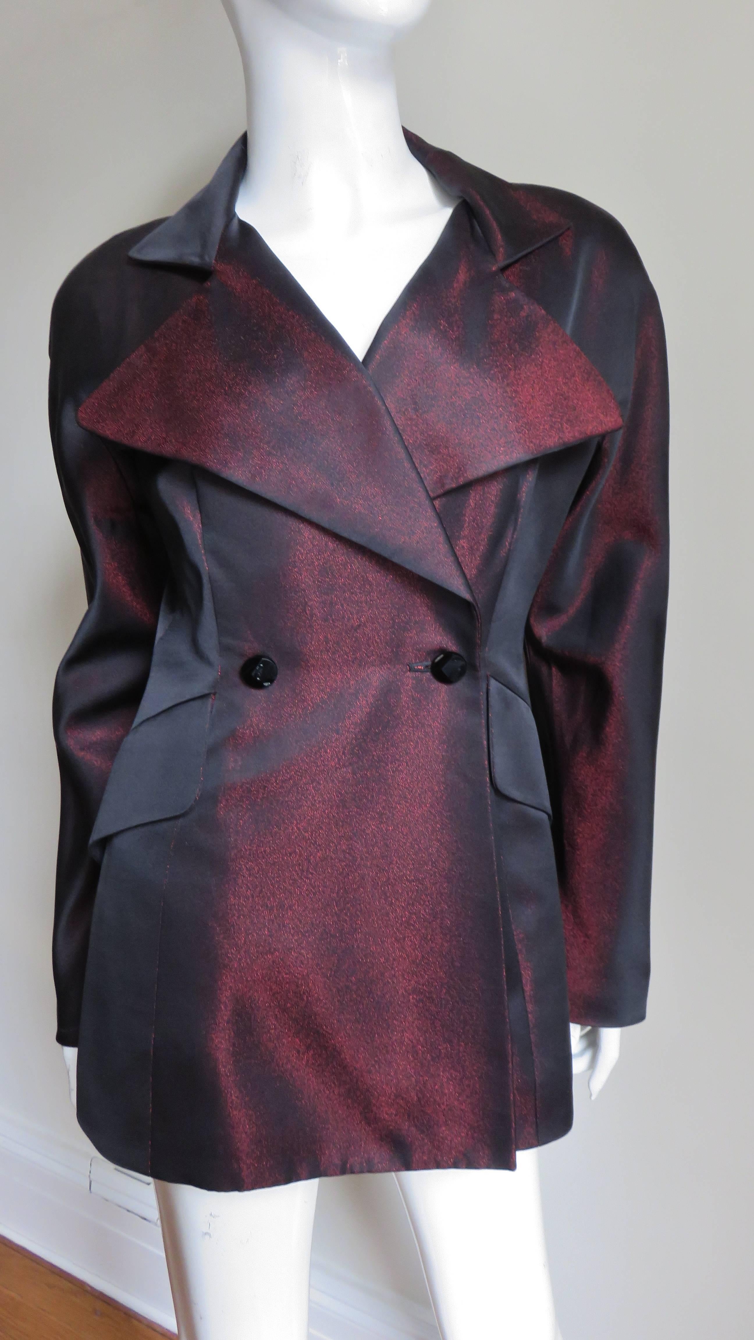 A fabulous iridescent burgundy and black silk blend jacket by Claude Montana. The peak lapel jacket is double breasted closing with front faceted black glass buttons. It has subtle dolman sleeves, 2 flap welt pockets in front and it is fully
