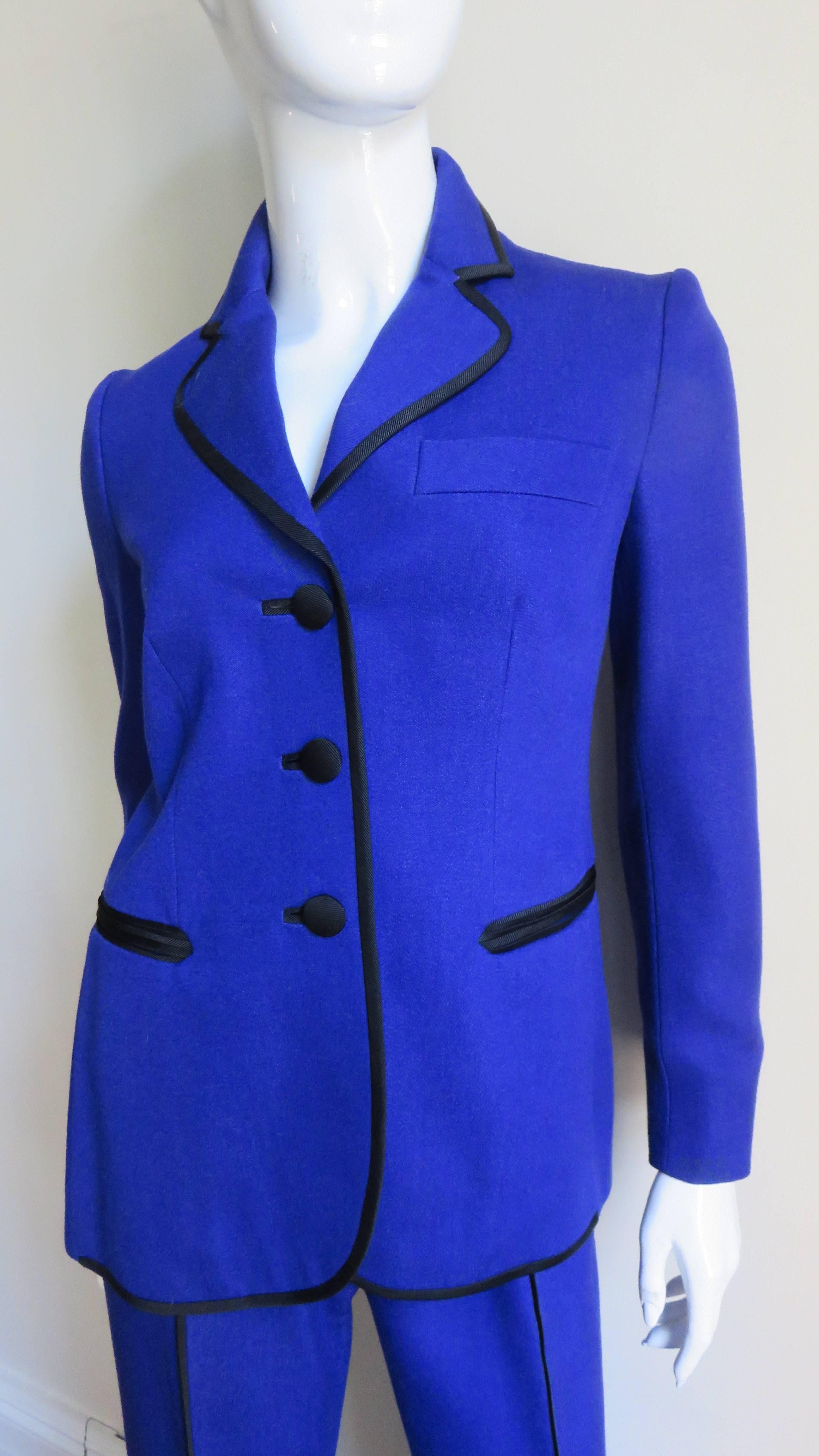 A fabulous fun pantsuit by Moschino in bright blue wool.  It consists of a boxy cut jacket and pants.  The jacket lapels, hem, welt pockets, center front and back pant legs and waistband are all trimmed in black braid.  The jacket has 3 front black