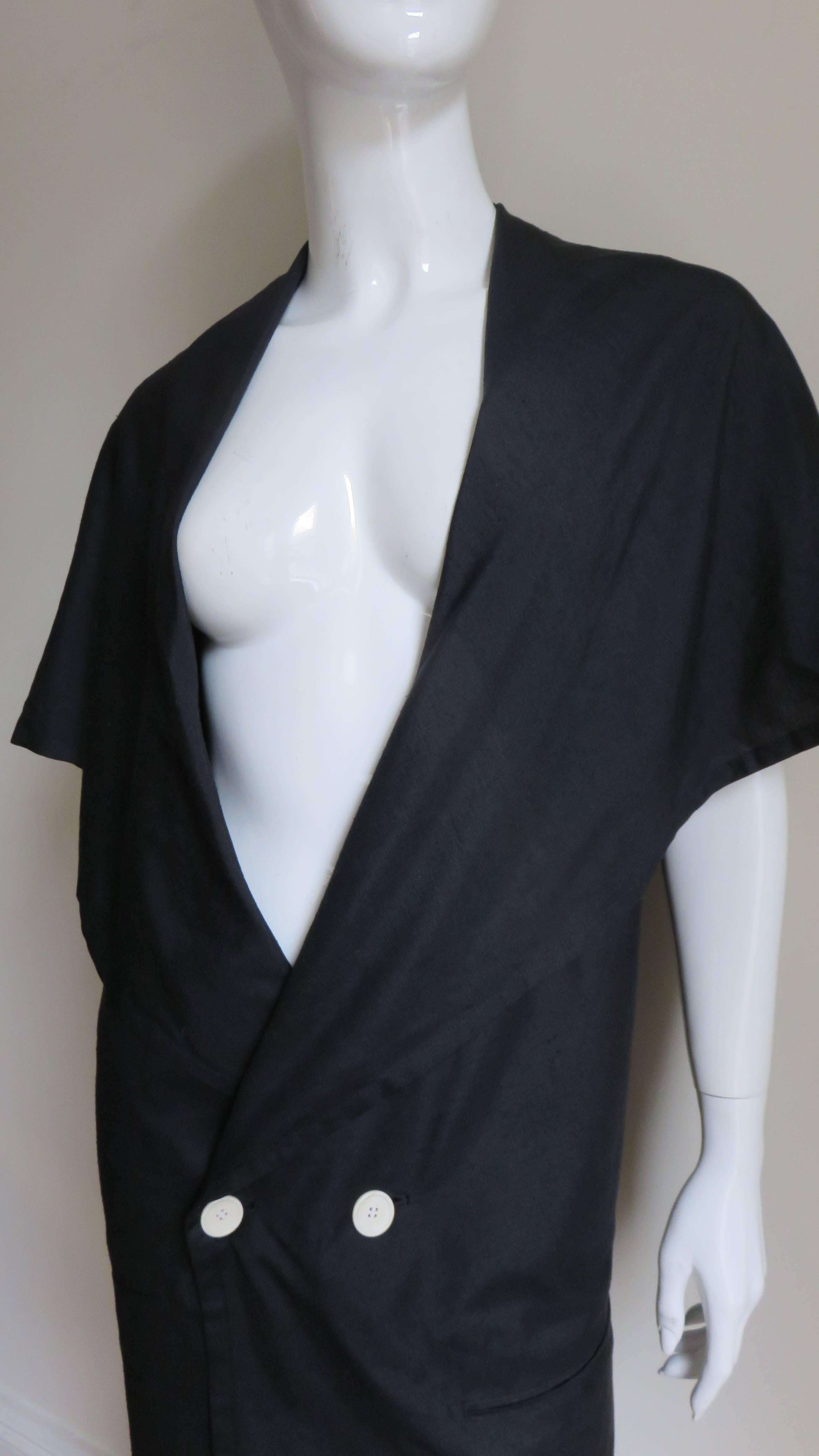 A fabulous black silk jacket from Yohji Yamamoto.  It is double breasted with 2 off white buttons and wide cape lapels which drape over the shoulders and upper arms.  This drape forms an asymmetric panel at the back long and pointed on one side and