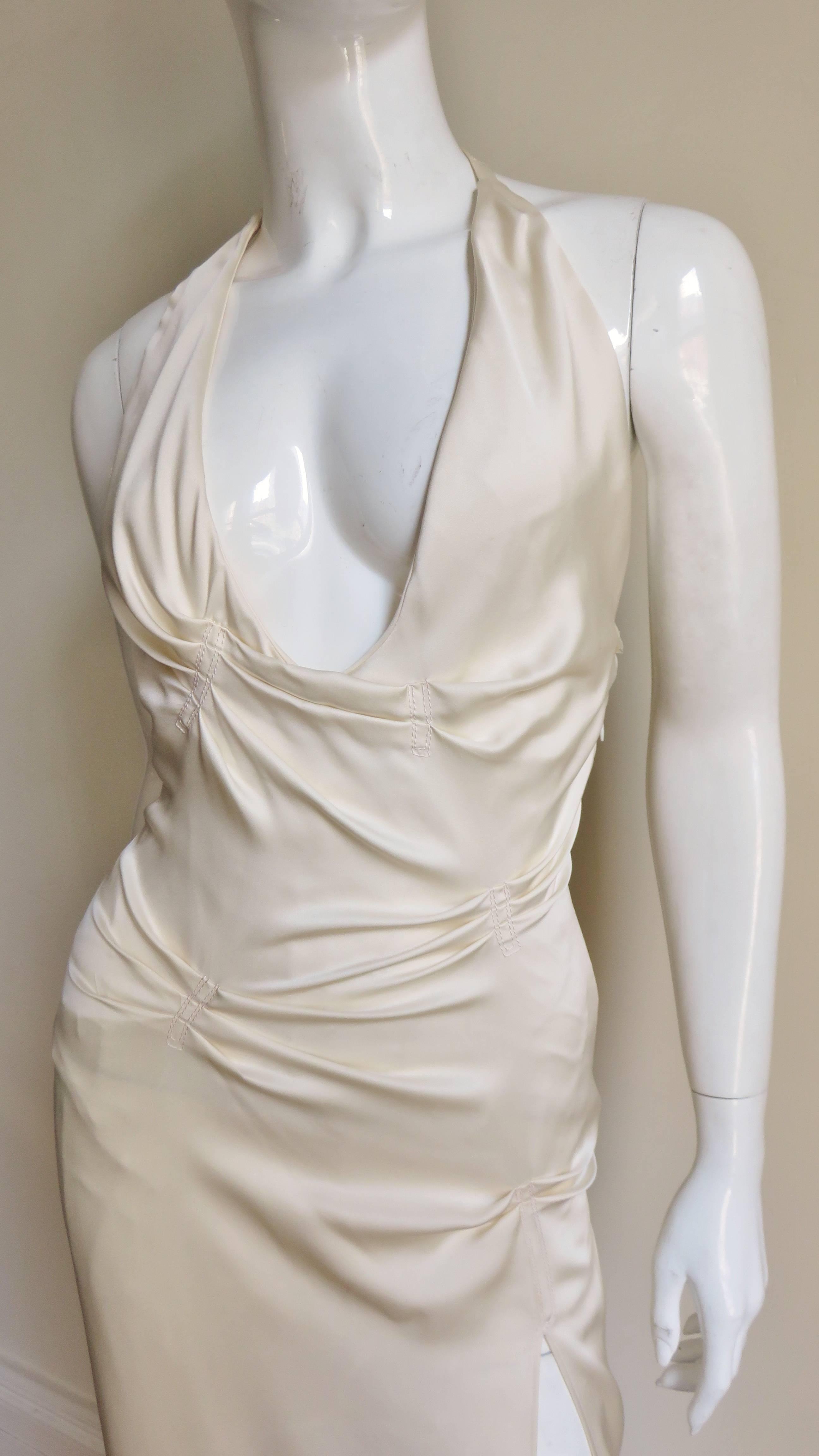 An incredible Ivory silk gown from Gianni Versace.  It is halter style with a plunging neckline and tucks placed off center at the bust waist and hips.  There is a thigh high slit along one leg revealing a white abstract line netting gore
