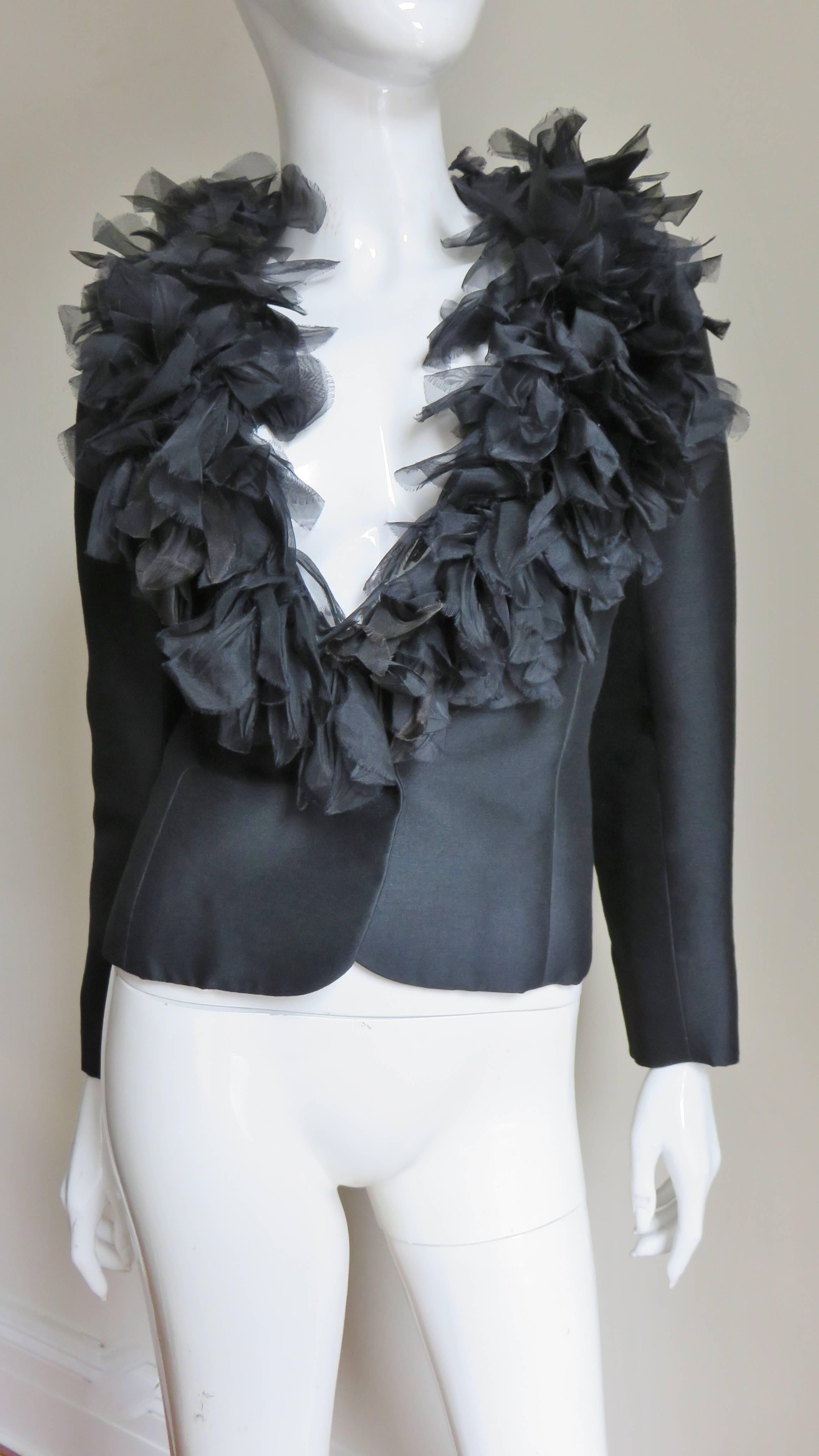 A beautiful black silk jacket by Junior Sophisticates.  It has a shawl collar generously adorned with semi sheer fluttering oblong silk organza applique strips and has princess seaming for an enhanced fit. There is one front self covered button