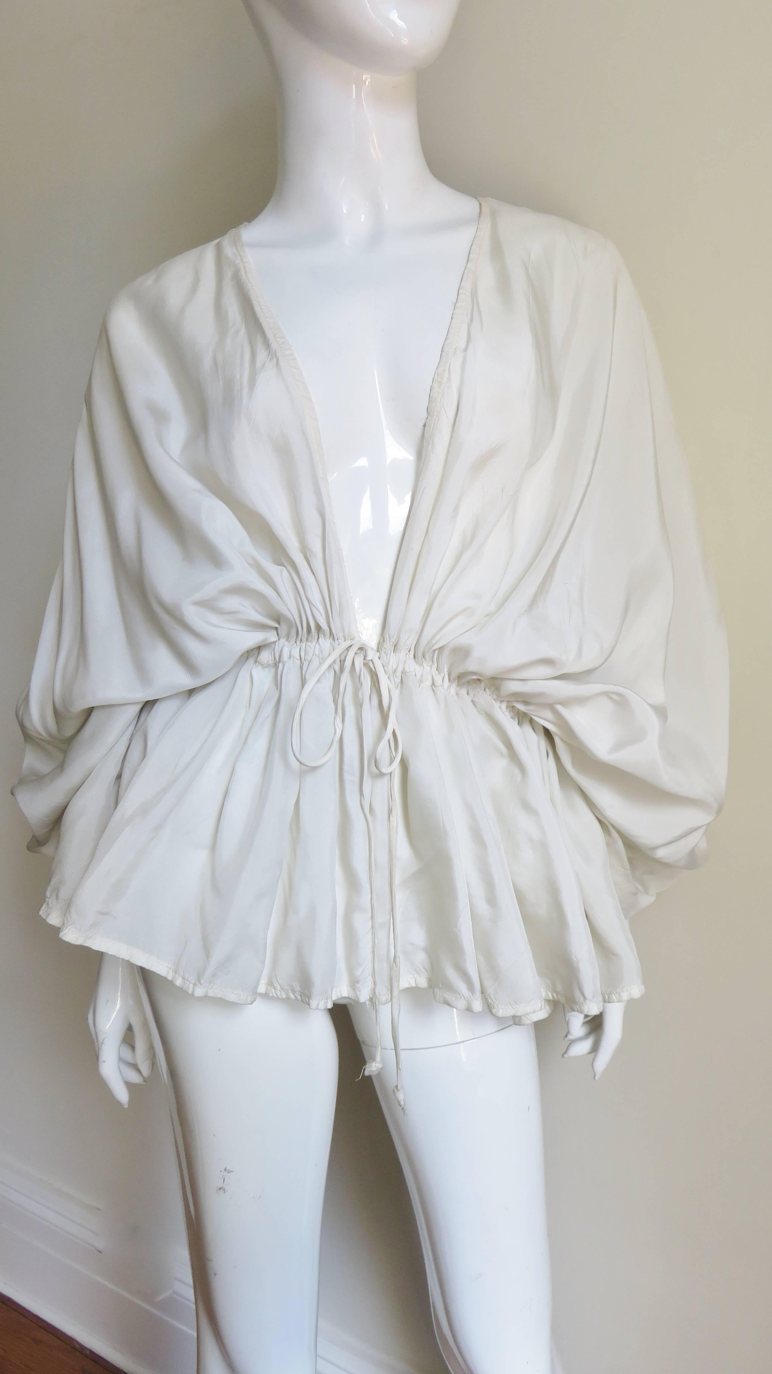 A pretty 1970's silk shirt with drawstring draped shoulders and a drawstring tie waist creating a full peplum.  The neckline is plunging to the waist.   VINTAGE SCHIECK
Excellent condition.  One size fits all.

Bust  Open
Waist  Open
Length  28"