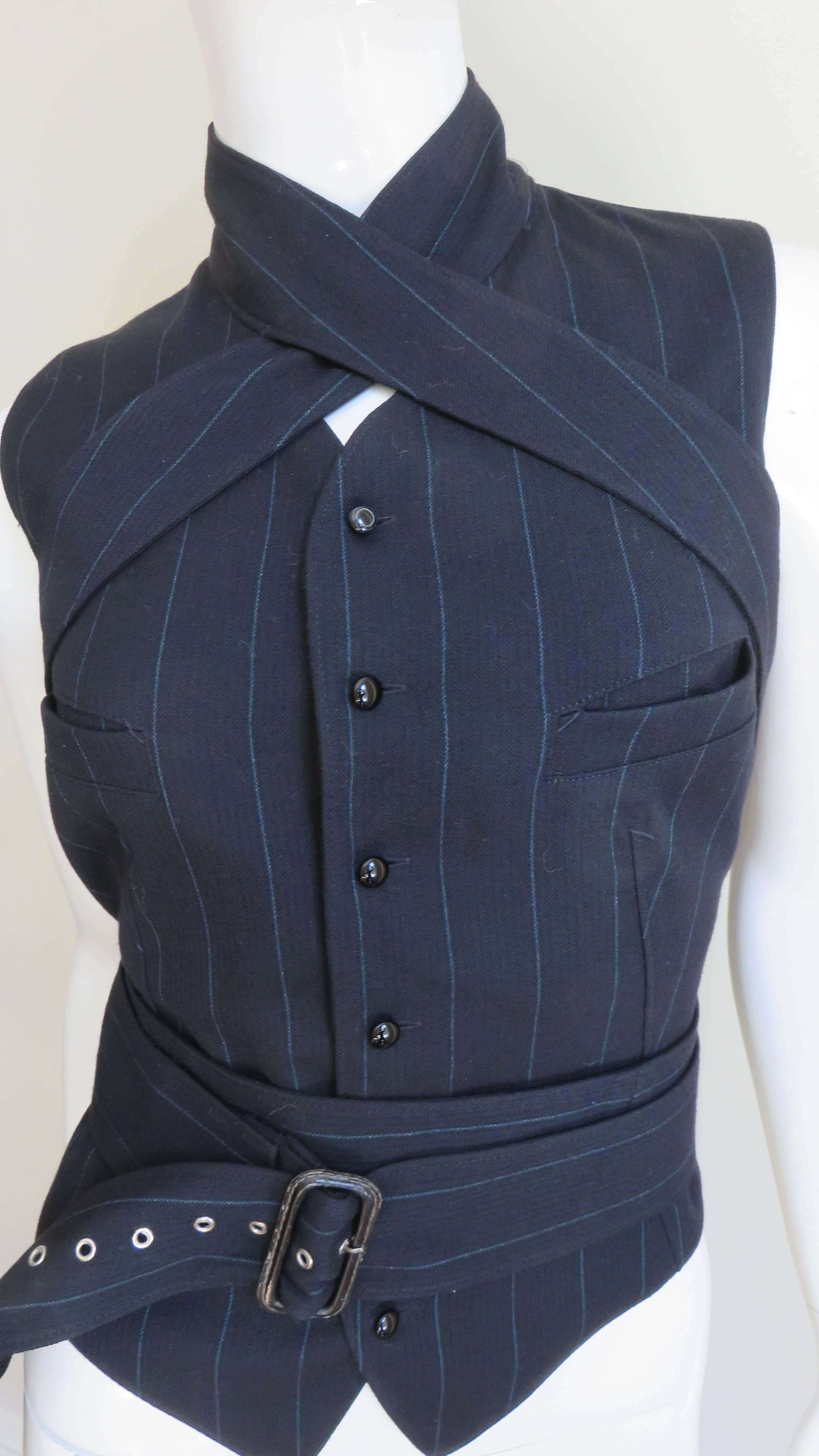 This is an incredible black with blue stripes wool vest by Jean Paul Gaultier.  It has a stand up collar from which extends to long straps with rings that wrap below the shoulders across the back and wrap once or twice around the waist closing with