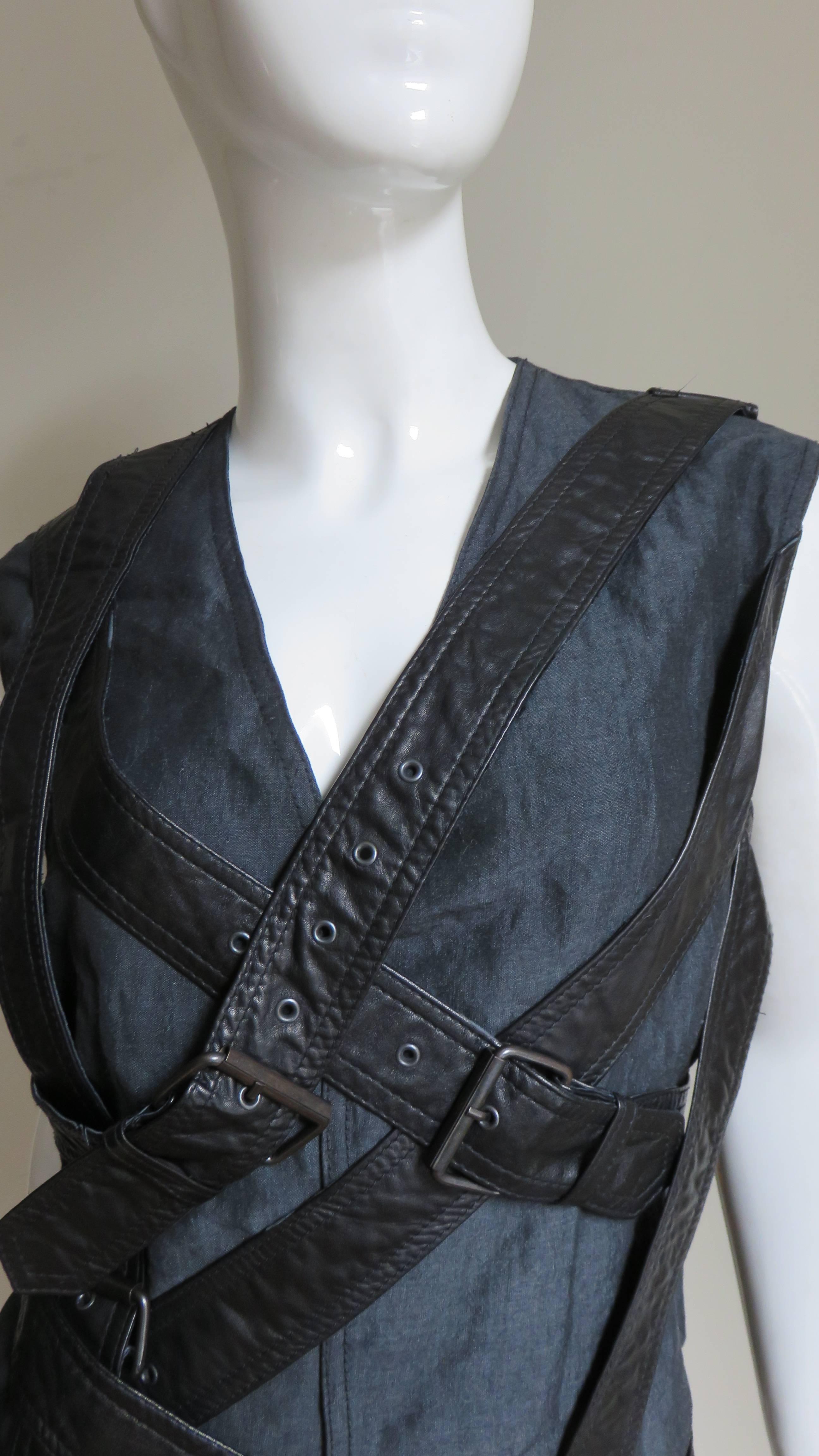 A fabulous black sleeveless jacket, vest, top attributed to Givenchy.  It is simple wrapping in front and completely adorned in functional, adjustable n PVC straps with buckles placed intermittently at various angles crossing the front and back.  It
