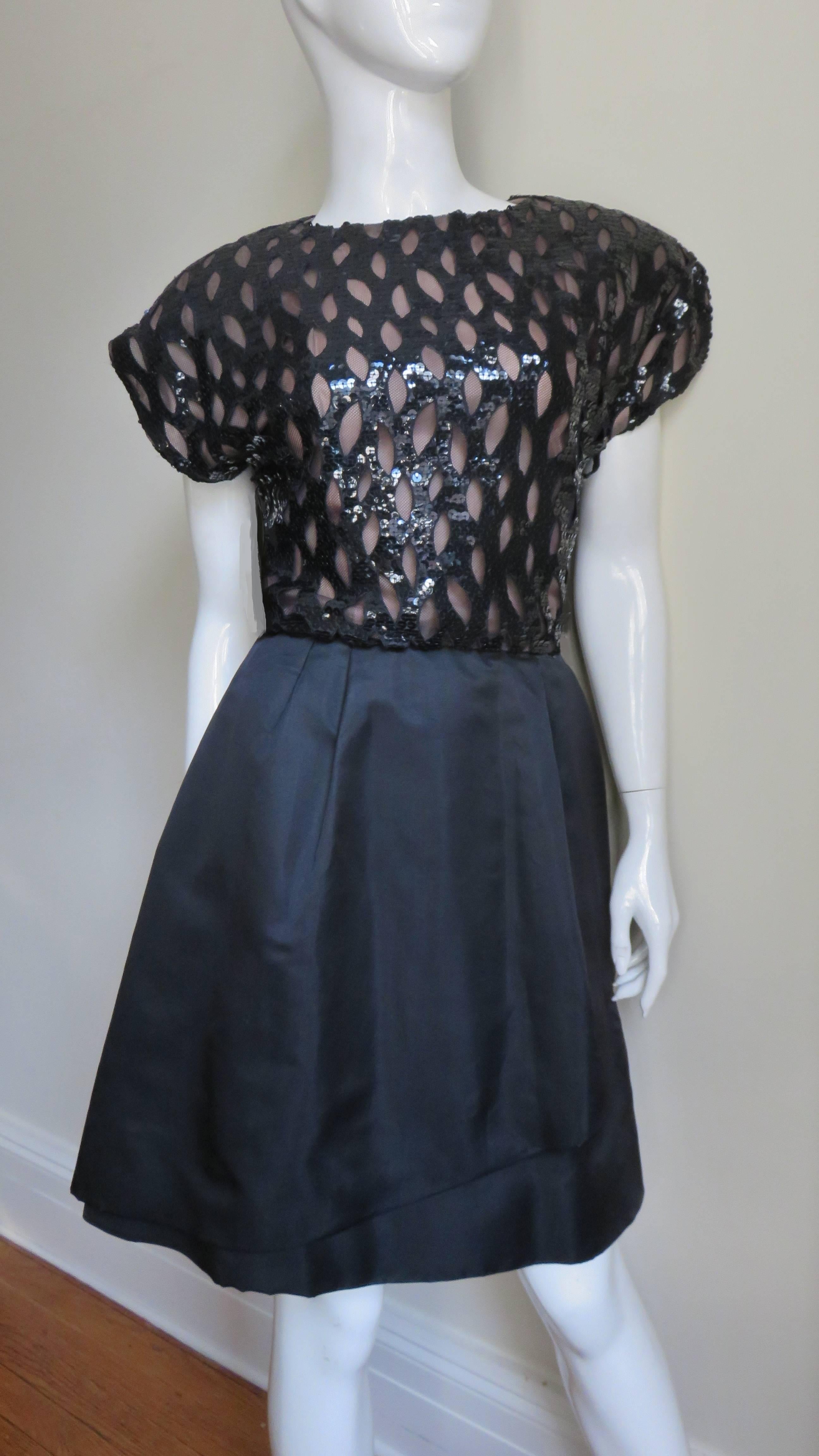 A fabulous black dress by Arnold Scassi. The bodice is comprised of a thatched sequin layer over a black mesh layer. It has a crew neck and extended shoulders forming cap sleeves. The skirt is lined in black silk, the shoulders are lightly padded
