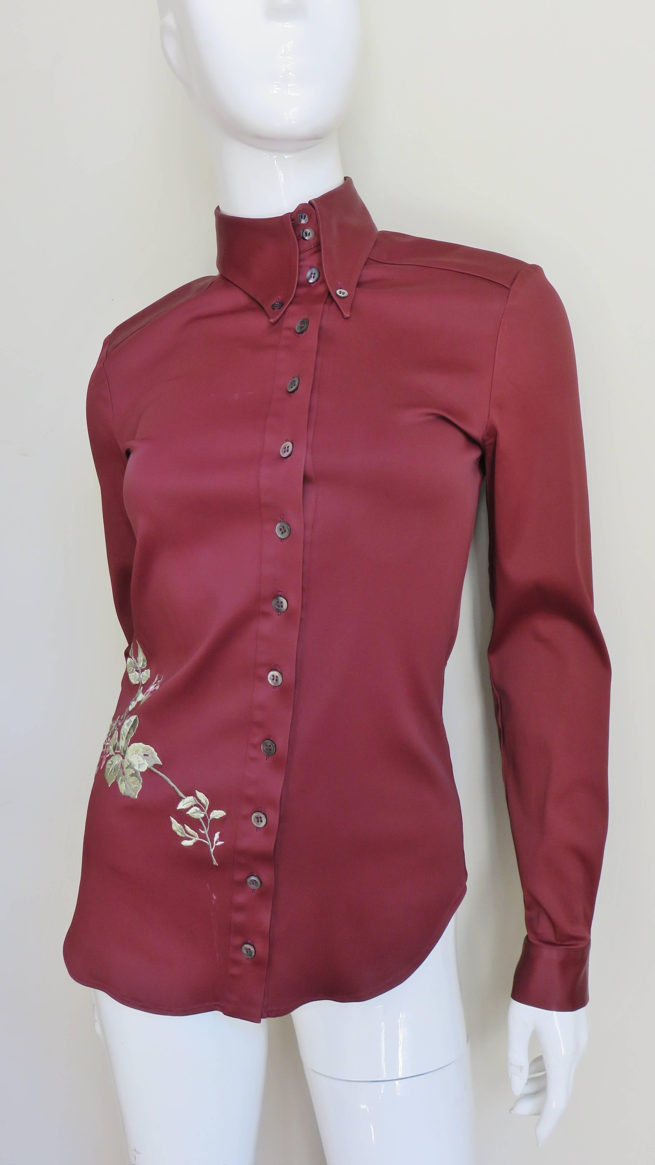 A beautiful wine stretch shirt by Alexander McQueen.  It is fitted with a shirt tail hem and a high button down shirt collar.  The  center is highlighted with beautiful, intricate, embroidered roses and leaves starting at the front of one hip