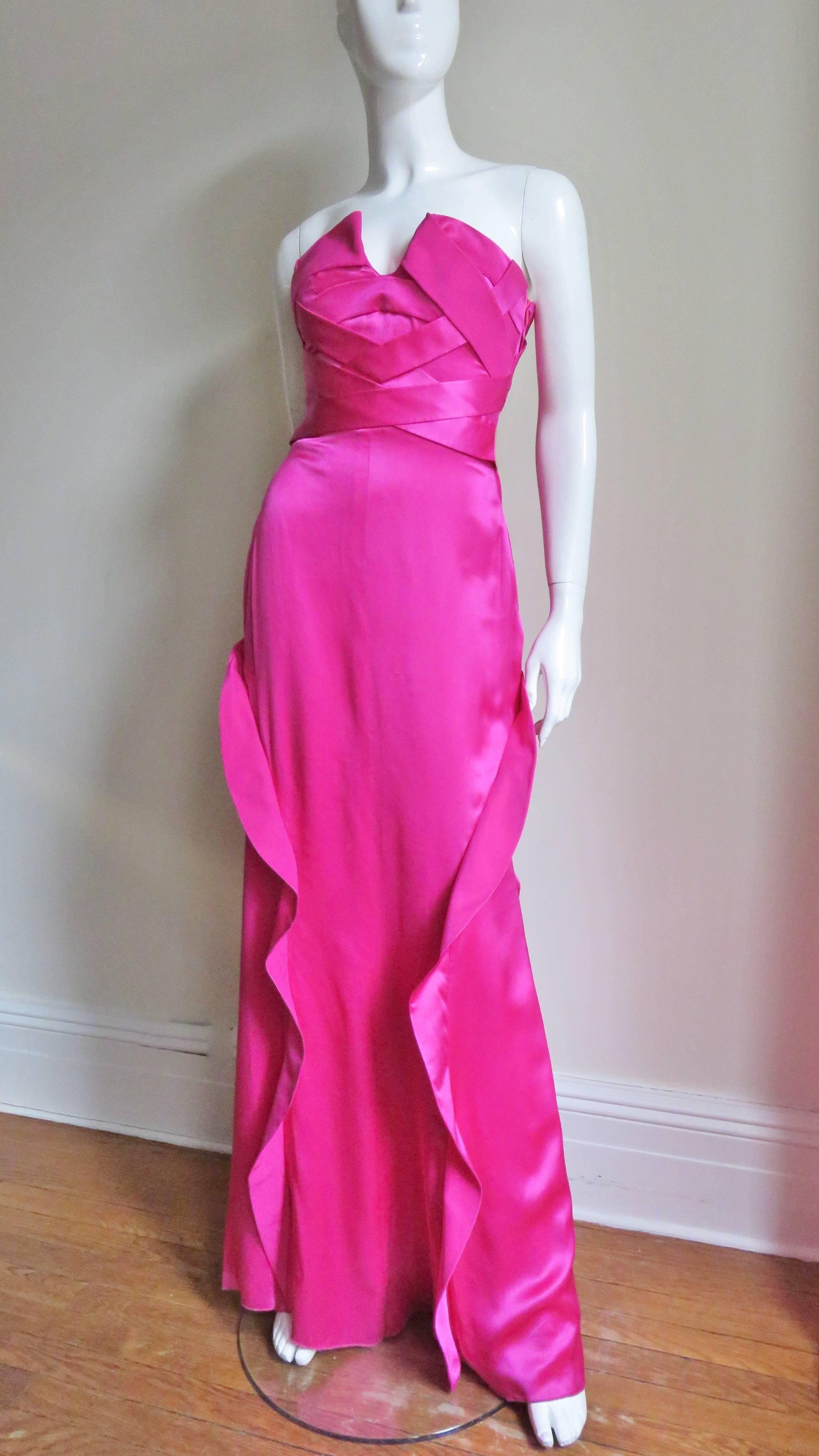 A gorgeous bright pink silk charmeuse strapless gown from Versace.  It has a fitted folding over at the bust with a center front plunge and bands criss crossing the front and back to the waist leaving a cutout below in the back.  The skirt portion