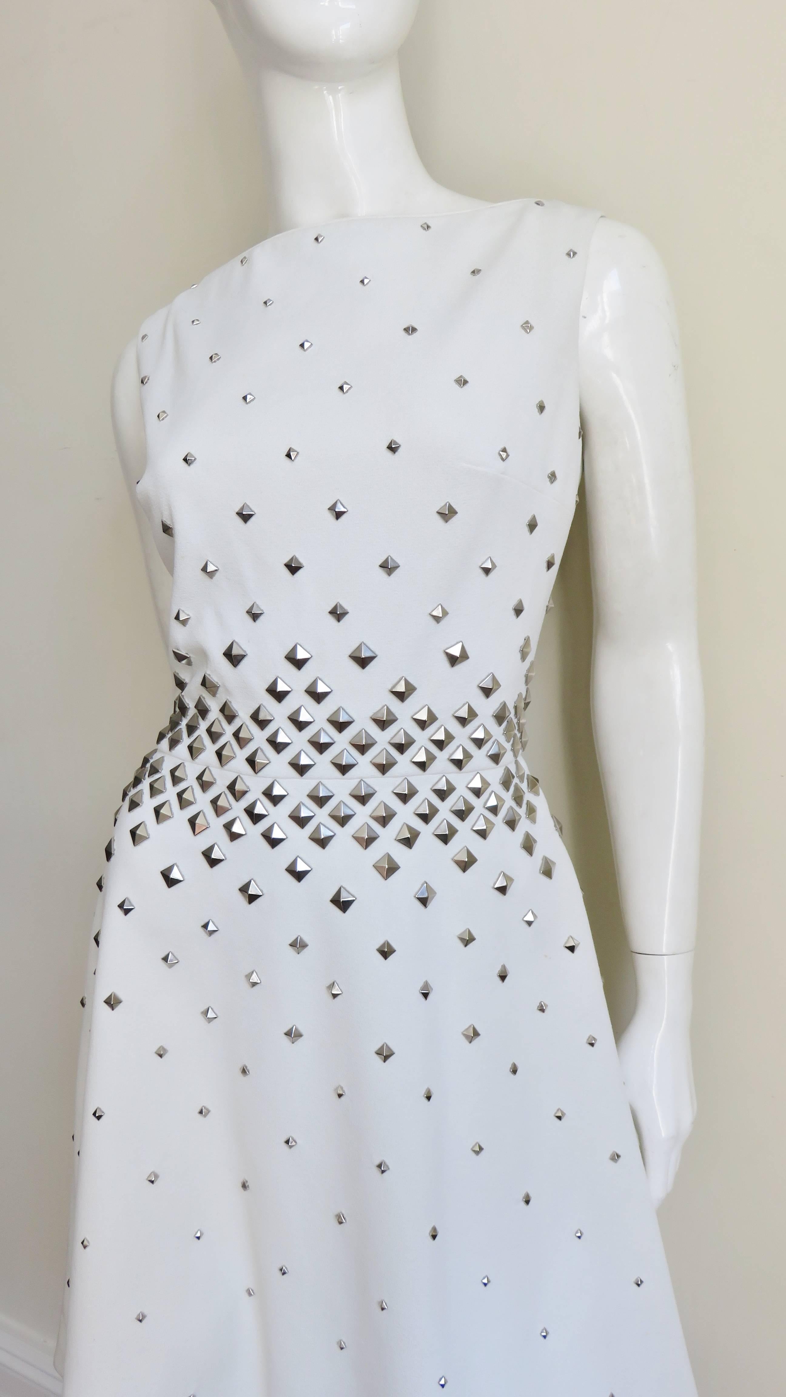 A great white jersey dress by Sydney North covered in silver studs.  It is sleeveless with a semi fitted waist and full skirt.  The waist is adorned with silver metal studs which decrease in size and spread out as they move away from the waist.  It