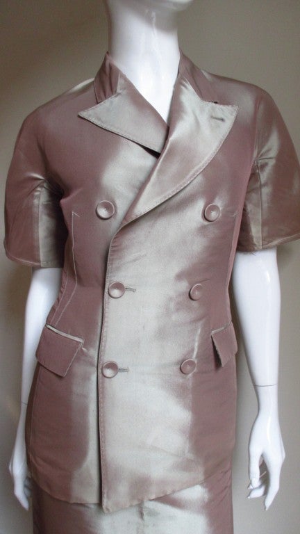 A skirt and jacket suit in iridescent blush silk  from Jean Paul Gaultier. The double breasted peak lapel jacket has short sleeves, 2 front welt flap pockets, 6 self covered buttons, hand stitching detail on the lapels and pocket flaps and fabulous