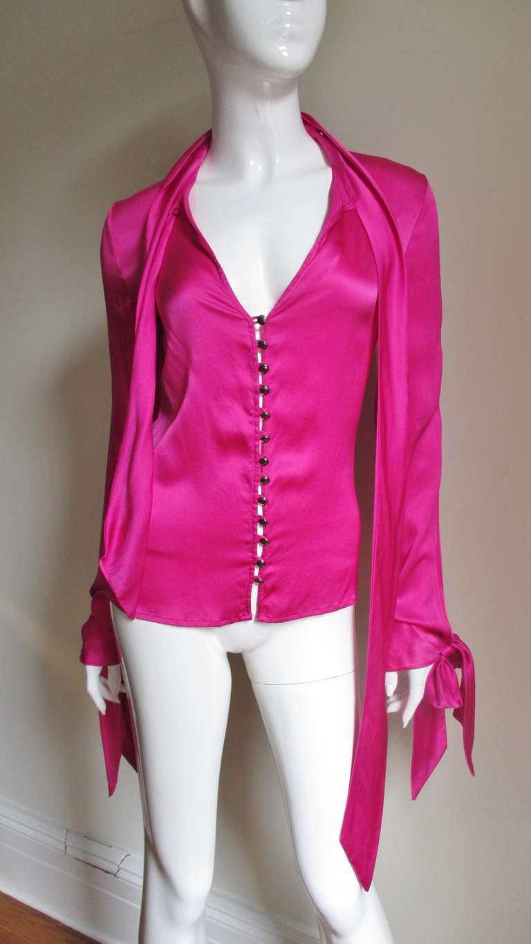 From Gianni Versace's Versus line a beautiful bright pink silk charmeuse shirt.  It is fitted through the waist and has a keyhole below a wrap neckline.  The sleeves have cuffs  which also have ties.  It is unlined and closes with Versus inscribed