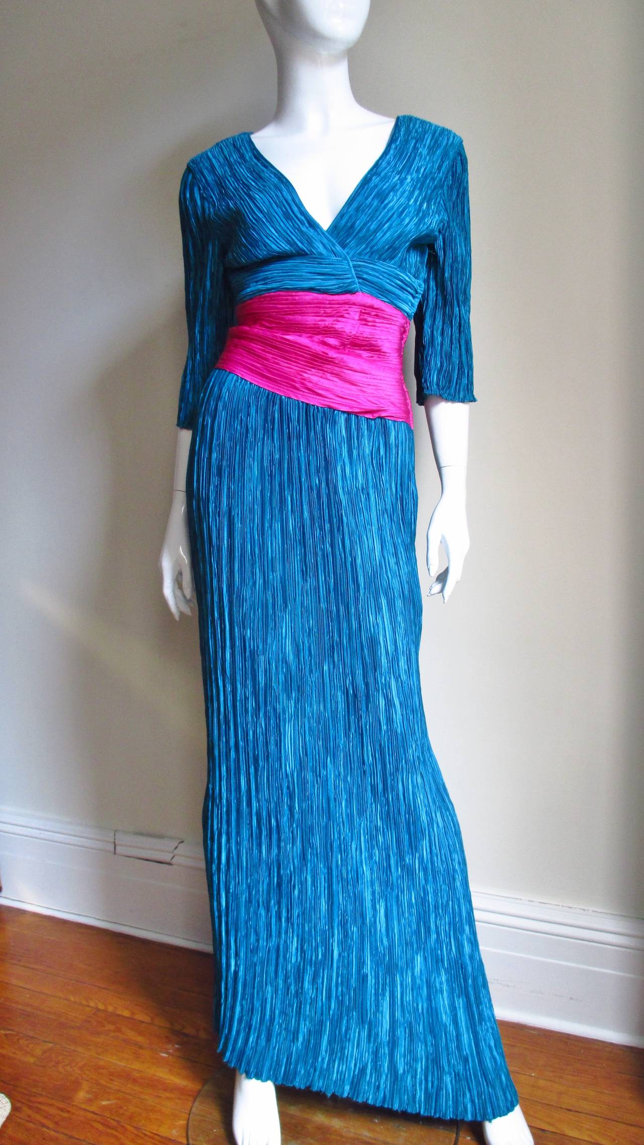 A beautiful turquoise and bright pink silk gown from Mary McFadden's Couture collection in her signature micro pleating. The bodice has a crossing plunging neckline front and back, elbow length sleeves and a bright pink horizontal band at the waist.