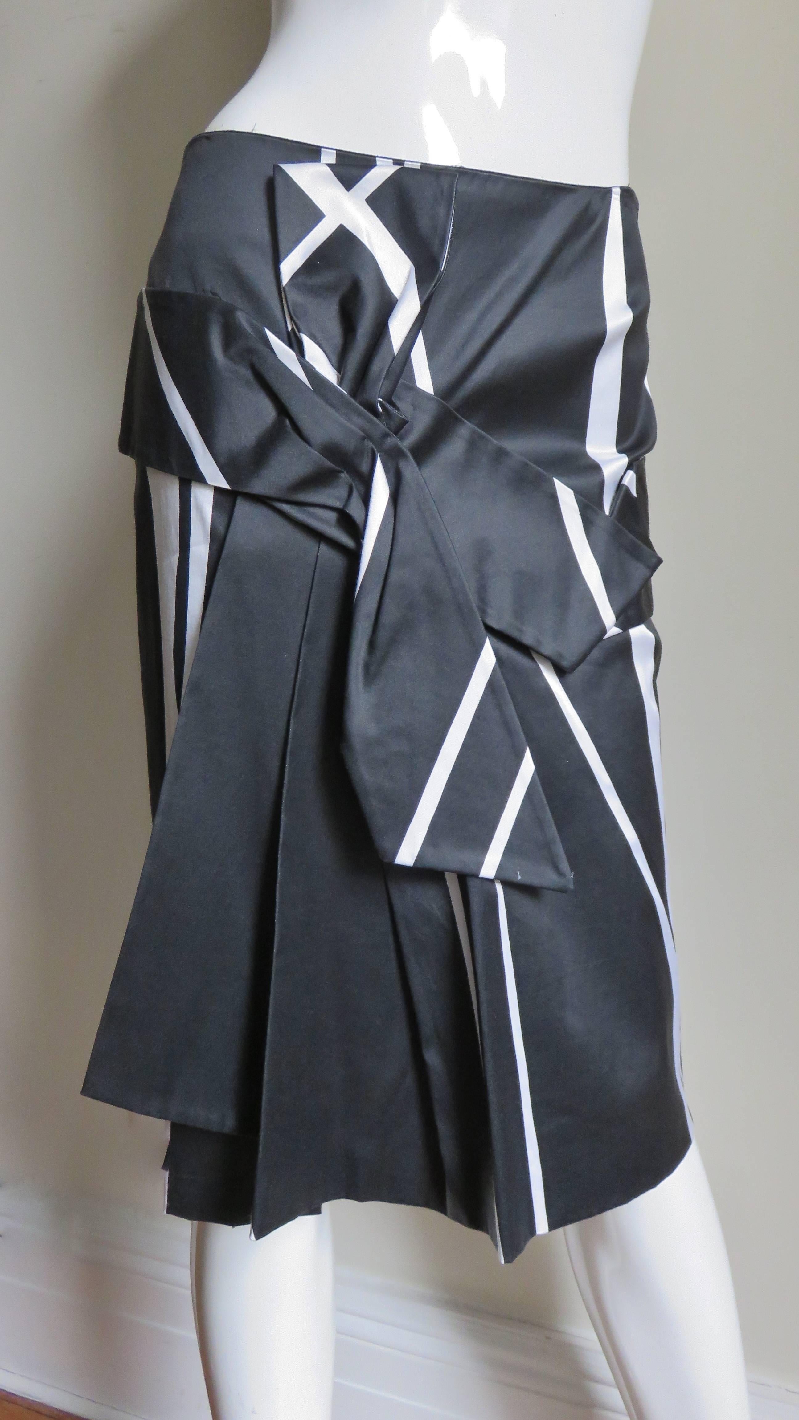 A pretty silk skirt by Martine Sitbon in an abstract pattern of intersecting off white stripes on a black background.  It has an a band around the hips forming an abstract tie off center front with a slit underneath.  It closes in the back with with