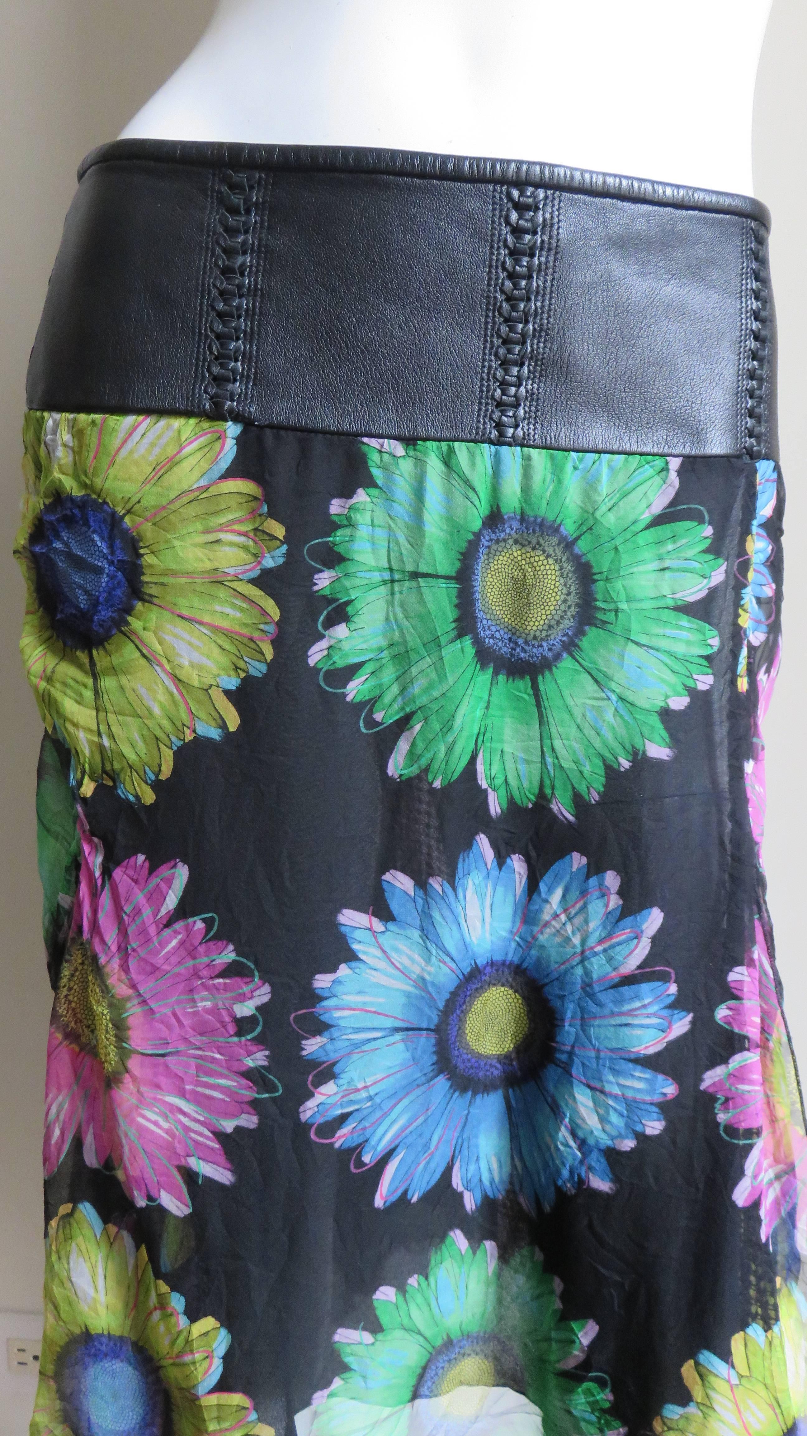 A gorgeous silk skirt with colorful flowers on a black background.  It has a wide leather waistband with inset inticately braided vertical lines.  The silk follows the line of the body with a black silk lining at the front and back leaving the sides