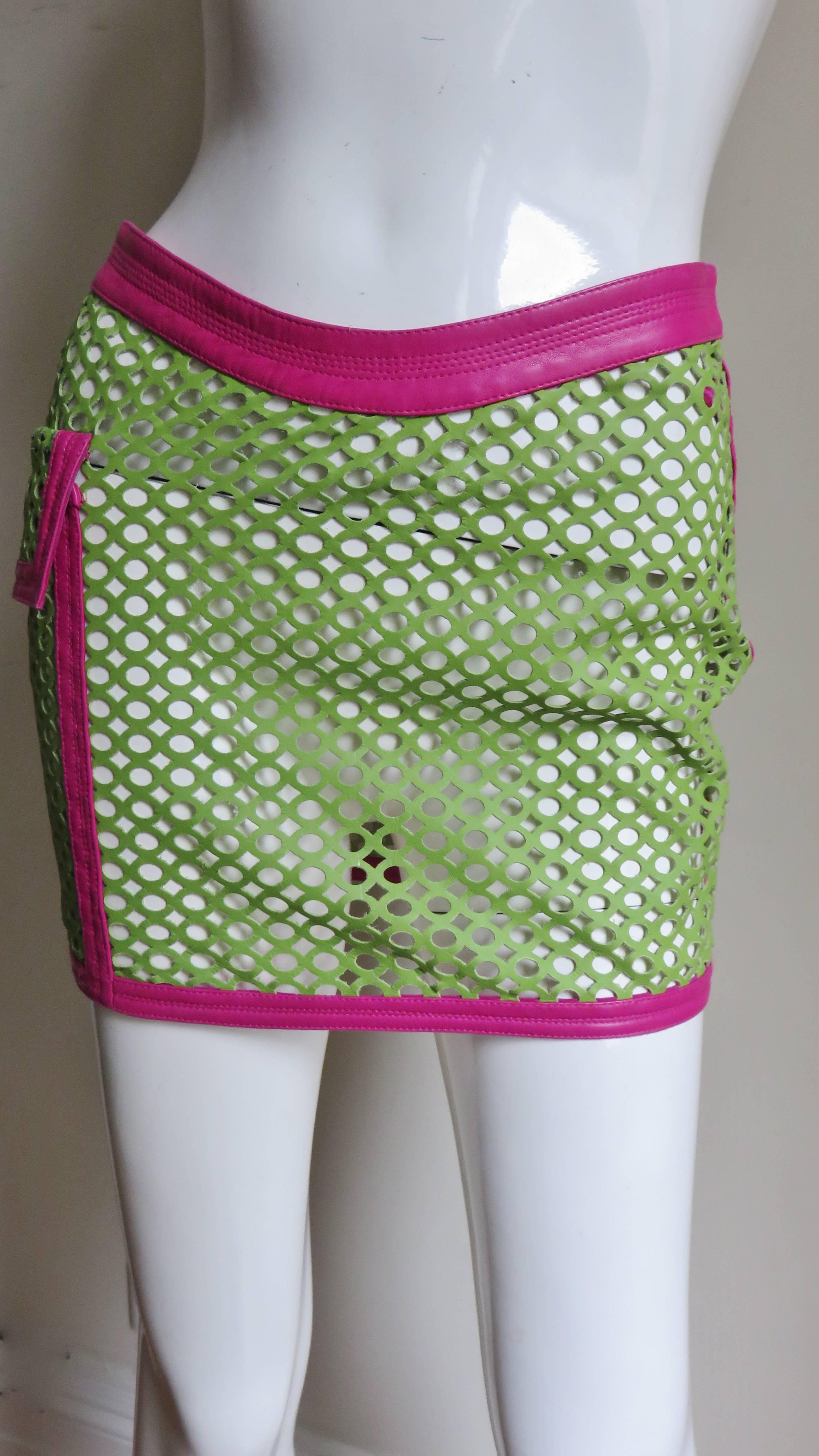 A perforated leather skirt in apple green trimmed in bright pink leather by Gianni Versace. The skirt has a curved waistband and a large functional flap patch pocket on one side framed in pink leather as is the hem, side seams and waistband. It has